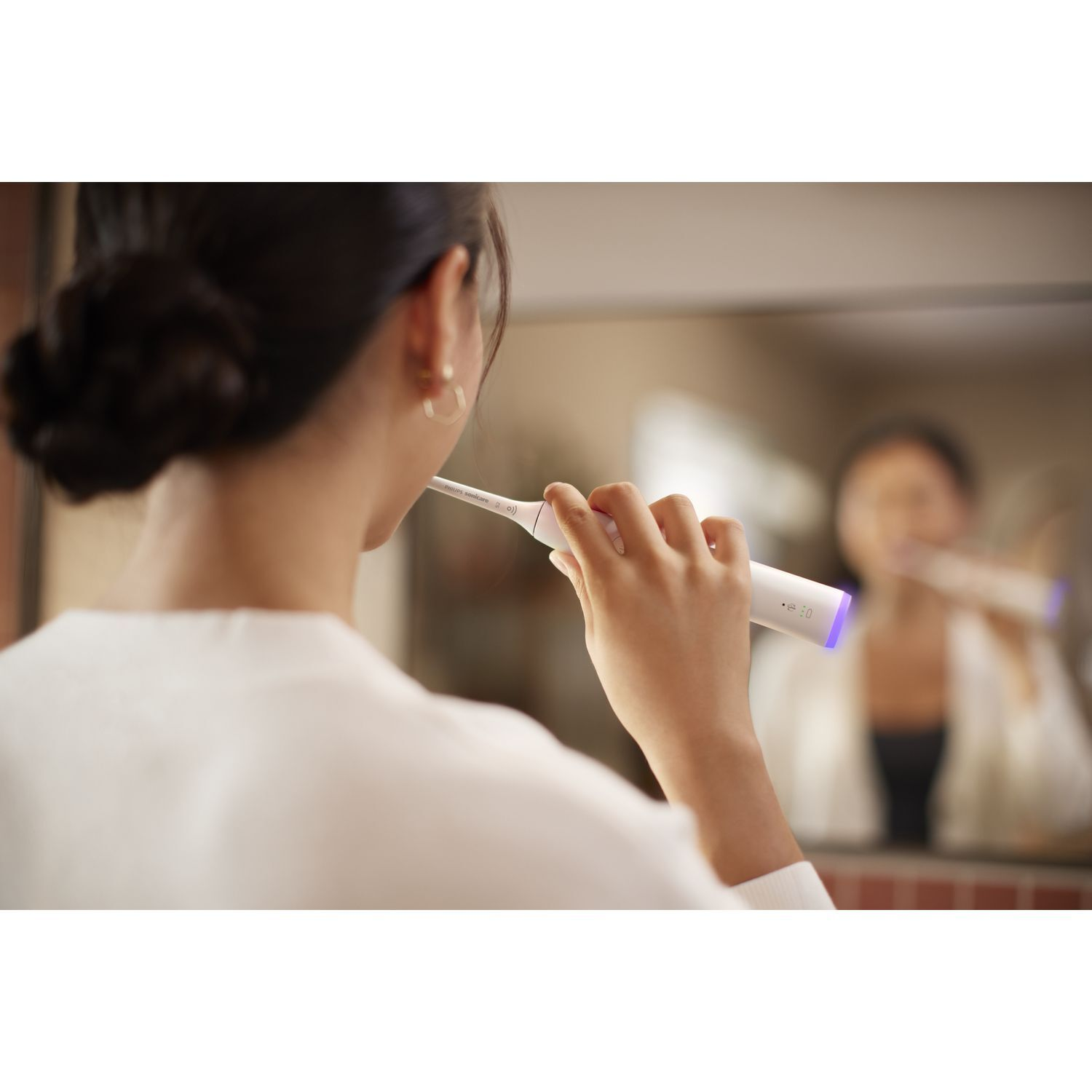 Femme se brossant les dents devant un miroir, reflet visible. Brosse à dents à la main.