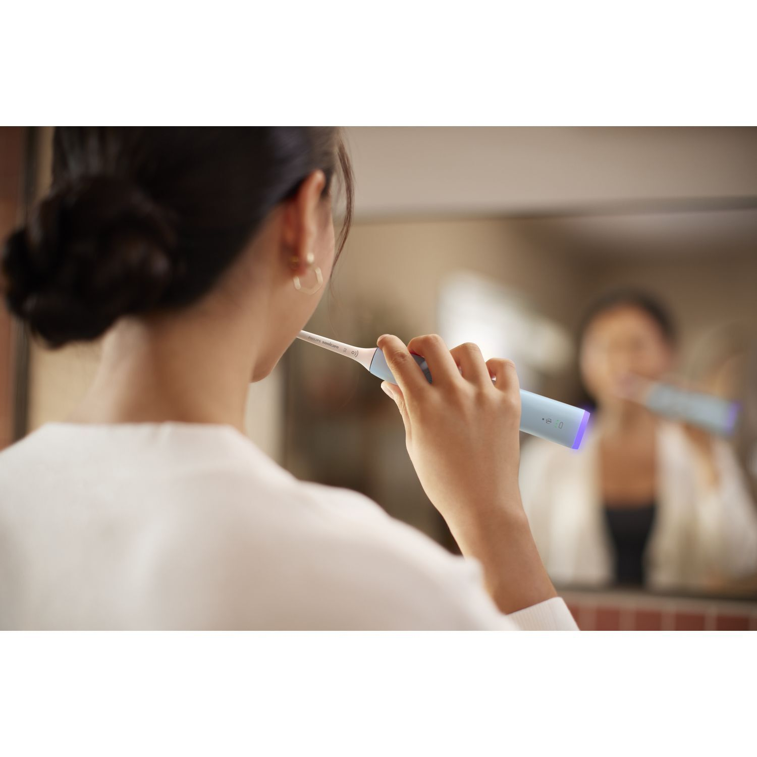 Femme se brossant les dents devant un miroir. Elle tient une brosse à dents bleue avec une lumière violette.