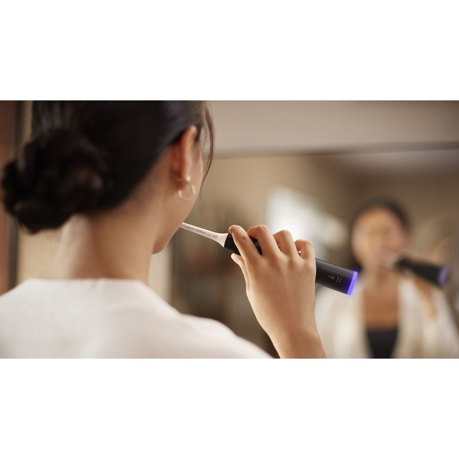 A woman brushing her teeth in front of a mirror with a Philips Sonicare toothbrush.