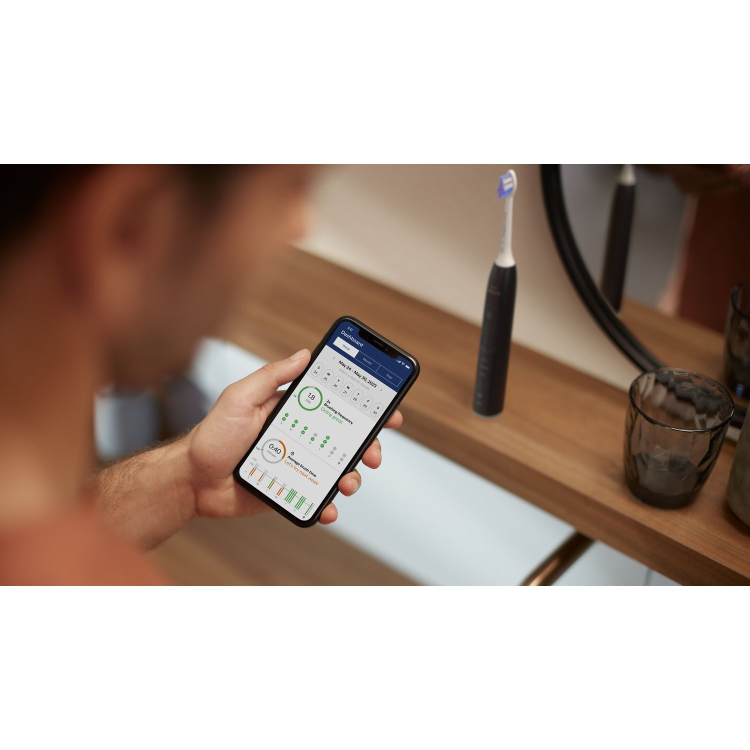Man using phone with toothbrush.  Phone shows brushing time and data. Bathroom setting. 
