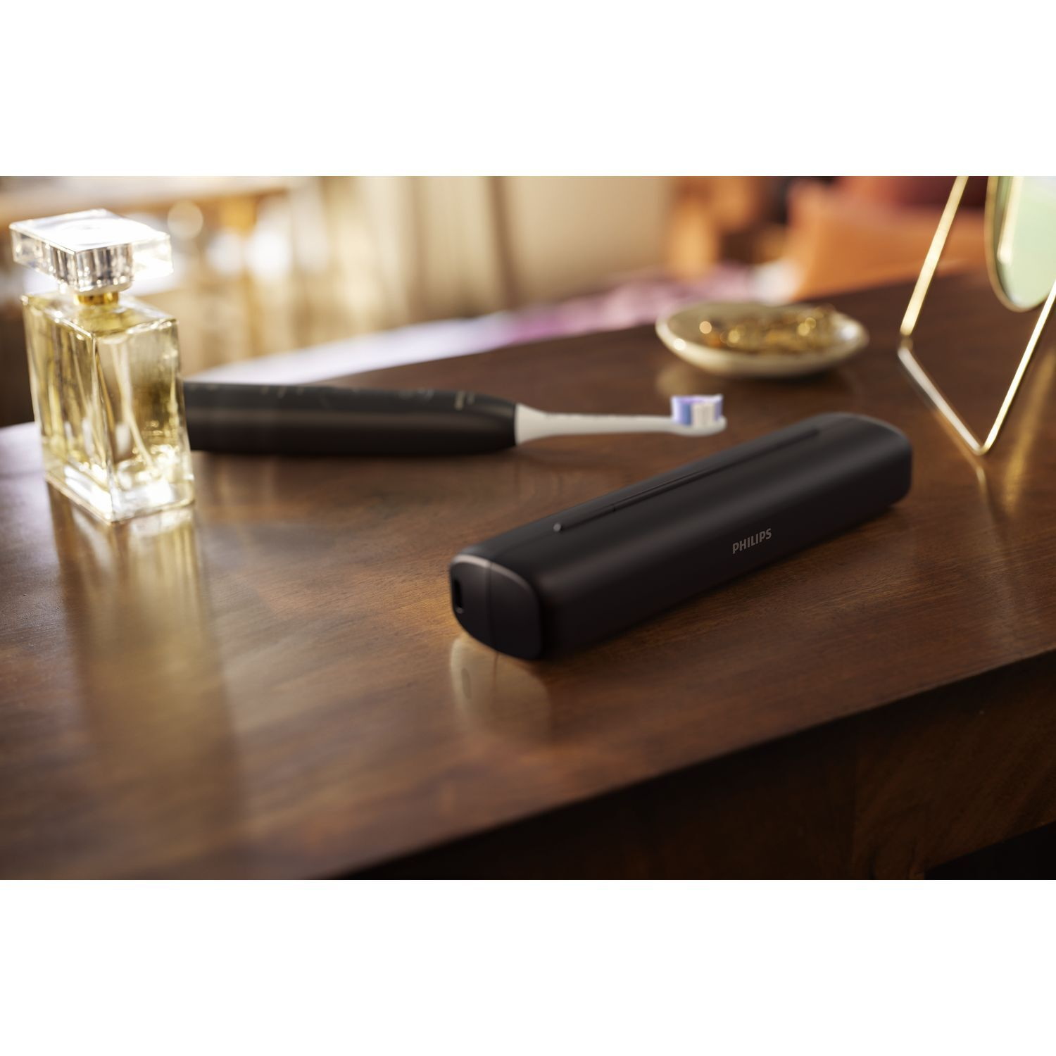 A black toothbrush, perfume bottle and a tray with jewelry on a wooden table.