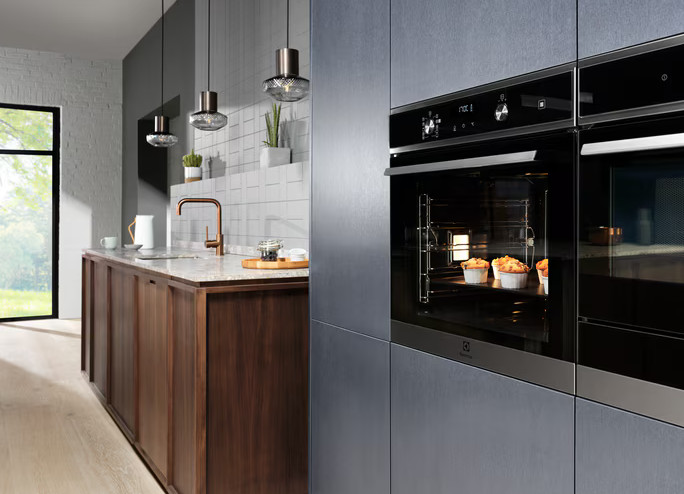 Nowoczesna kuchnia z niebieskimi szafkami. Piekarnik z babeczkami jest na pierwszym planie.