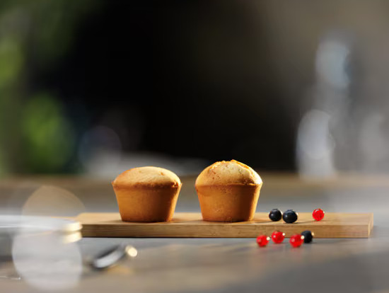 Dwie babeczki na drewnianej desce z borówkami i czerwonymi jagodami.