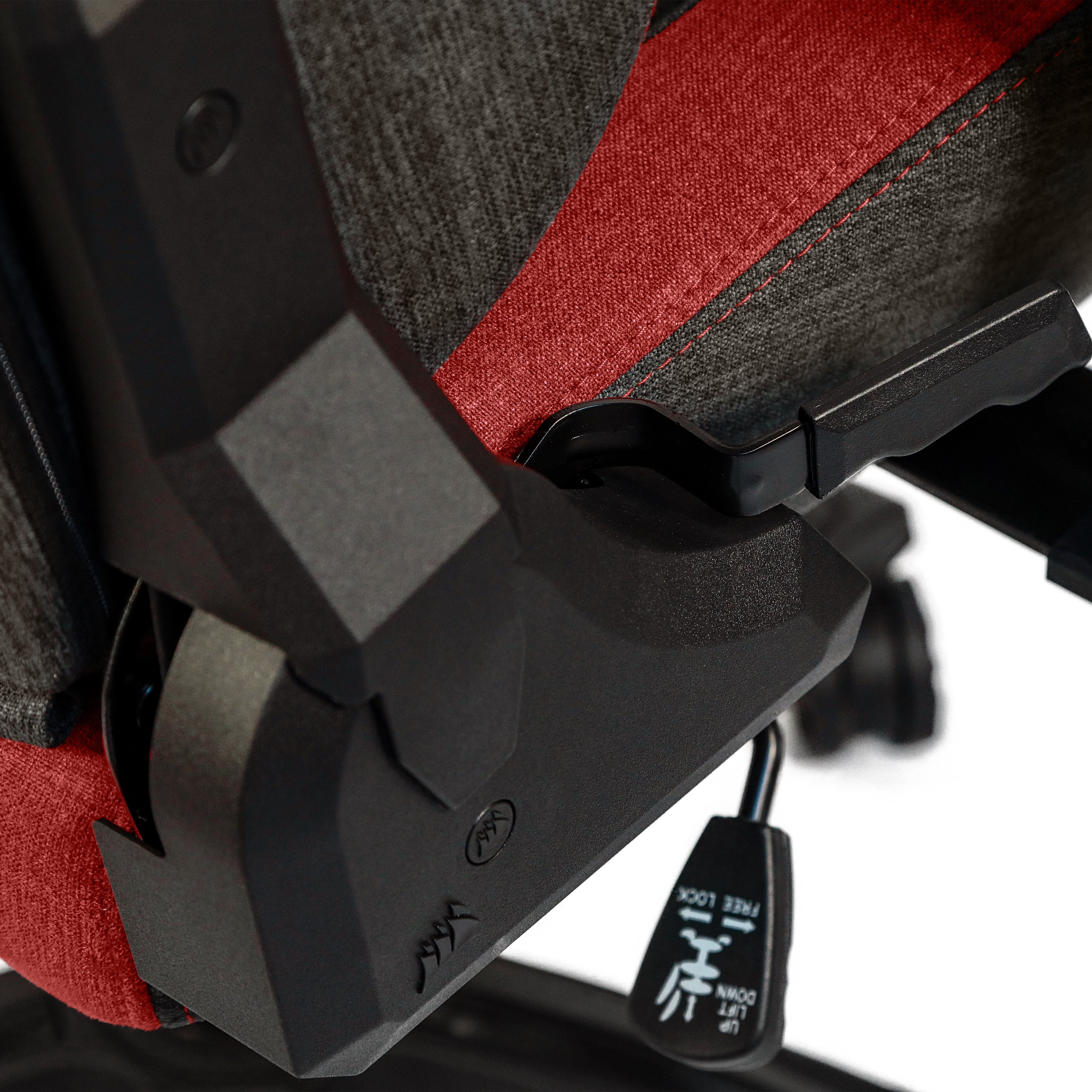 Zbliżenie mechanizmu fotela do gier. Widoczne: czarna dźwignia, czerwona tkanina i symbol blokady/odblokowania.