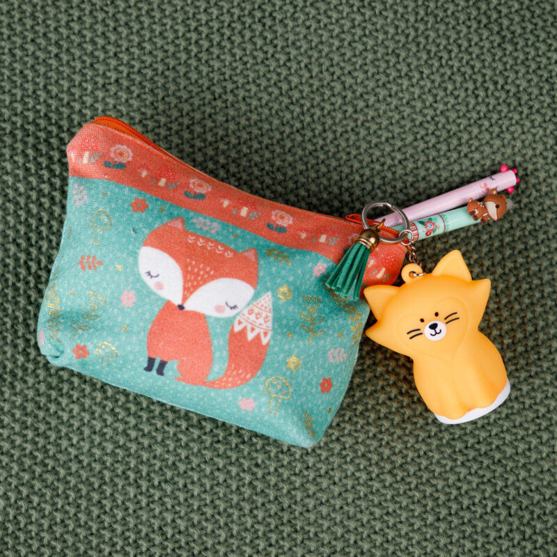 Mała portmonetka z motywem lisa, brelokiem z lisem i dwoma długopisami na zielonej powierzchni.