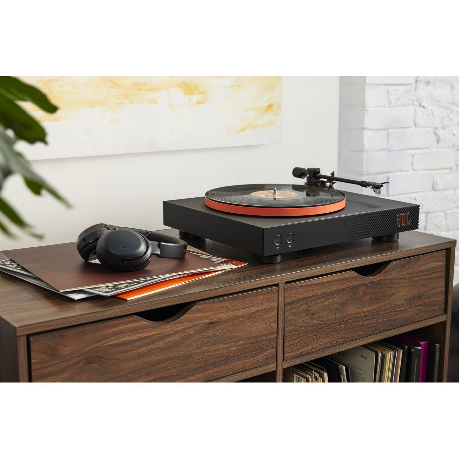 Platenspeler met een oranje ring op een houten kast met een plaat en koptelefoon.