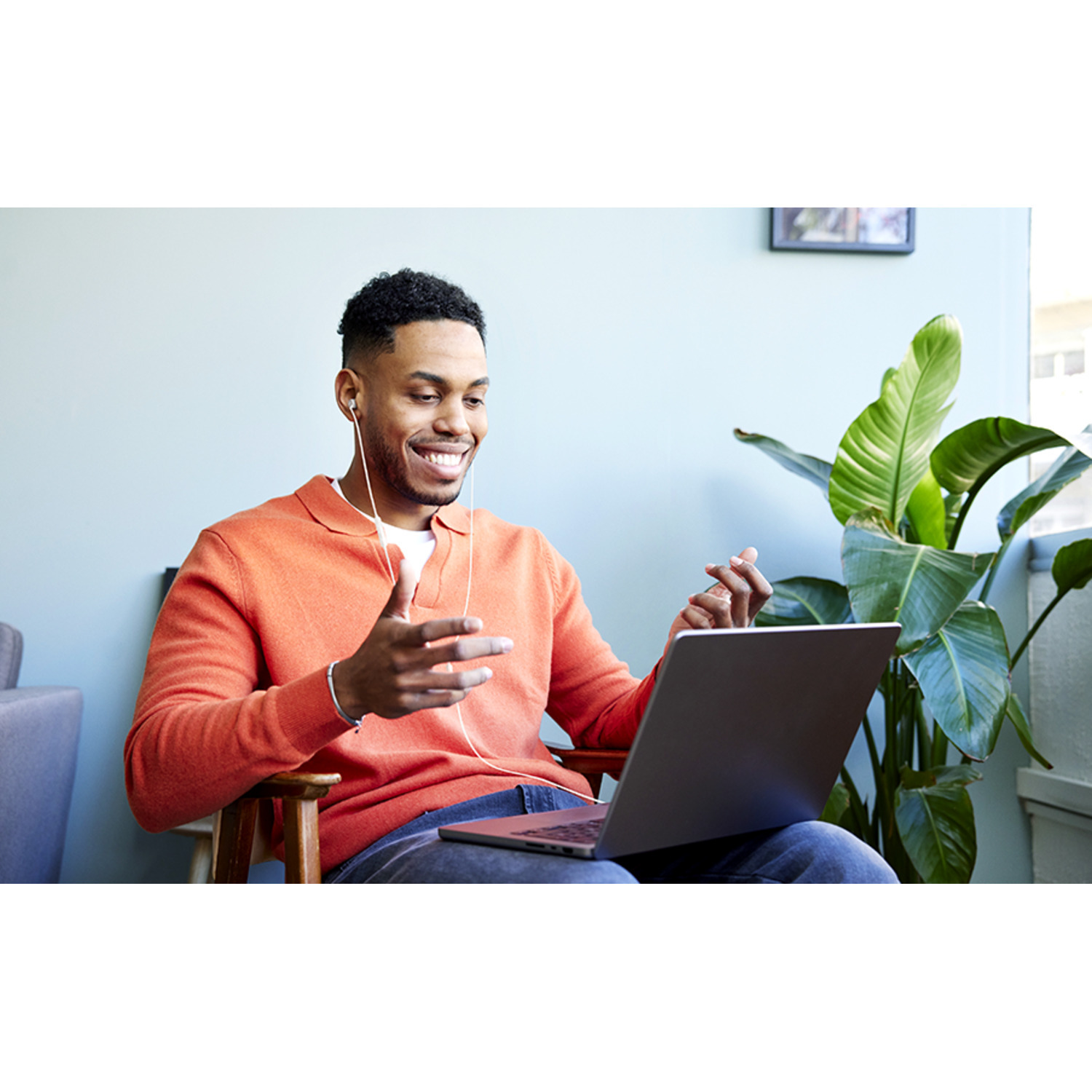 Man in oranje trui lacht tijdens videogesprek op een laptop.