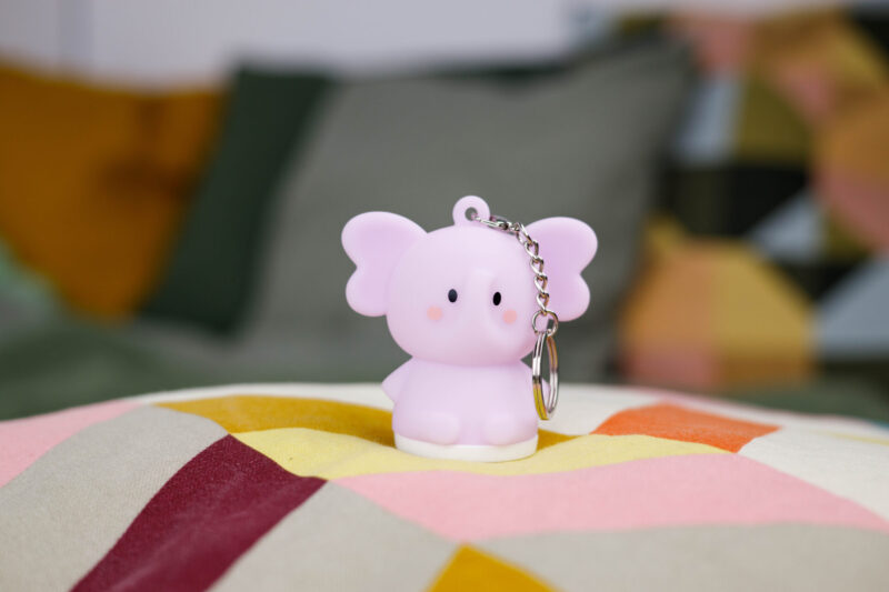 Różowy brelok w kształcie słonia na kolorowej poduszce, tło rozmyte.