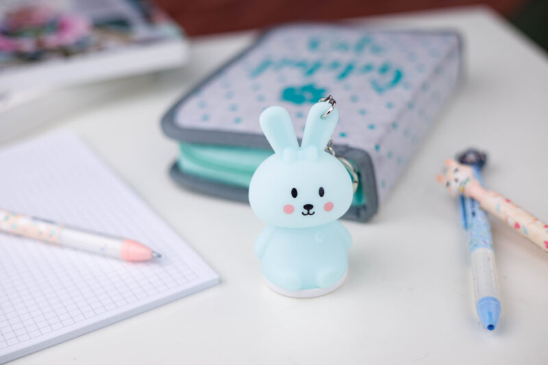 Niebieski breloczek z królikiem na stole z długopisami i piórnikiem.