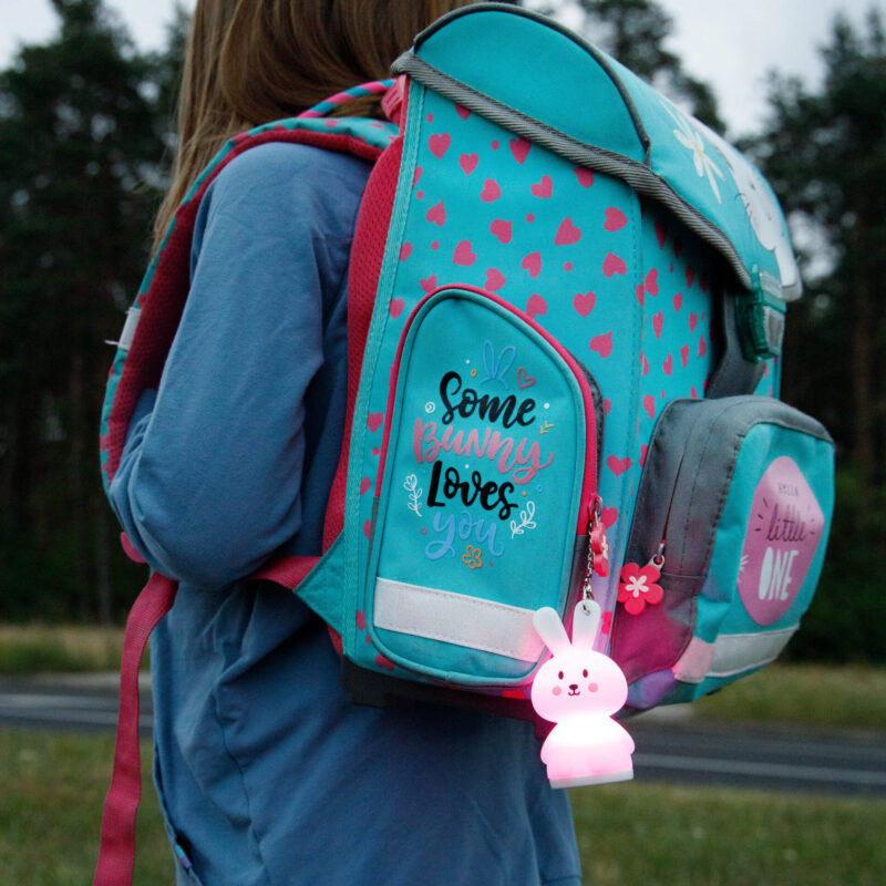 Dziecko z turkusowym plecakiem ze światłem w kształcie królika. Plecak ma różowe serca i tekst.