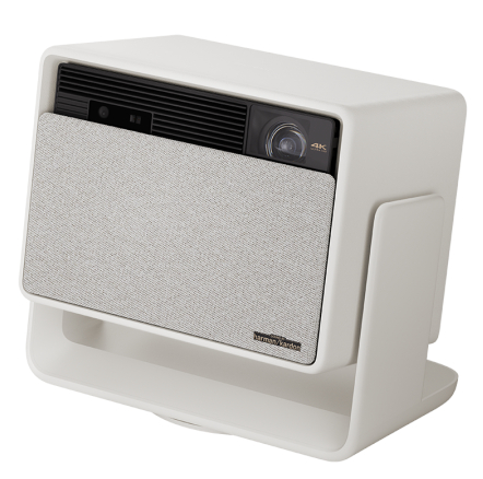 Biały projektor z głośnikiem pokrytym tkaniną i czarnym panelem przednim. Jest ustawiony pod kątem na białym stojaku.