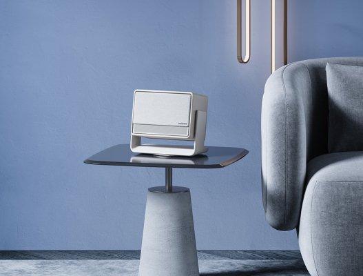 Biały głośnik na stole. Szara sofa w tle. Niebieska ściana.