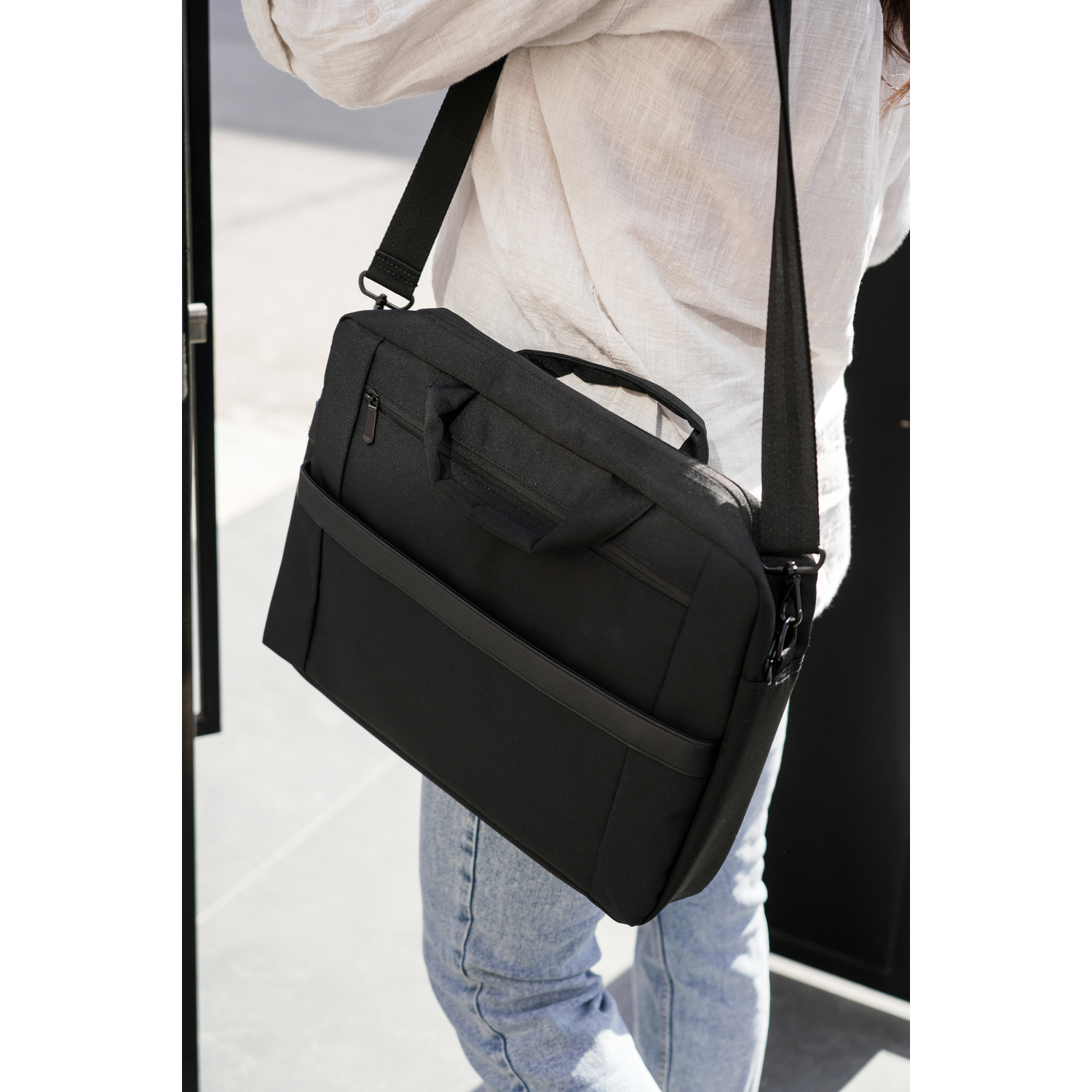 A person carrying a black messenger bag over their shoulder. They are wearing a white shirt and jeans.