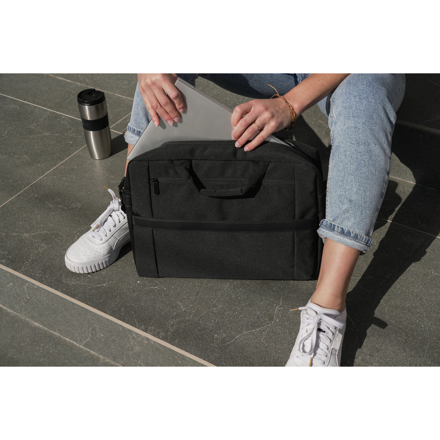 Person putting a laptop into a black bag, with a mug on the floor.