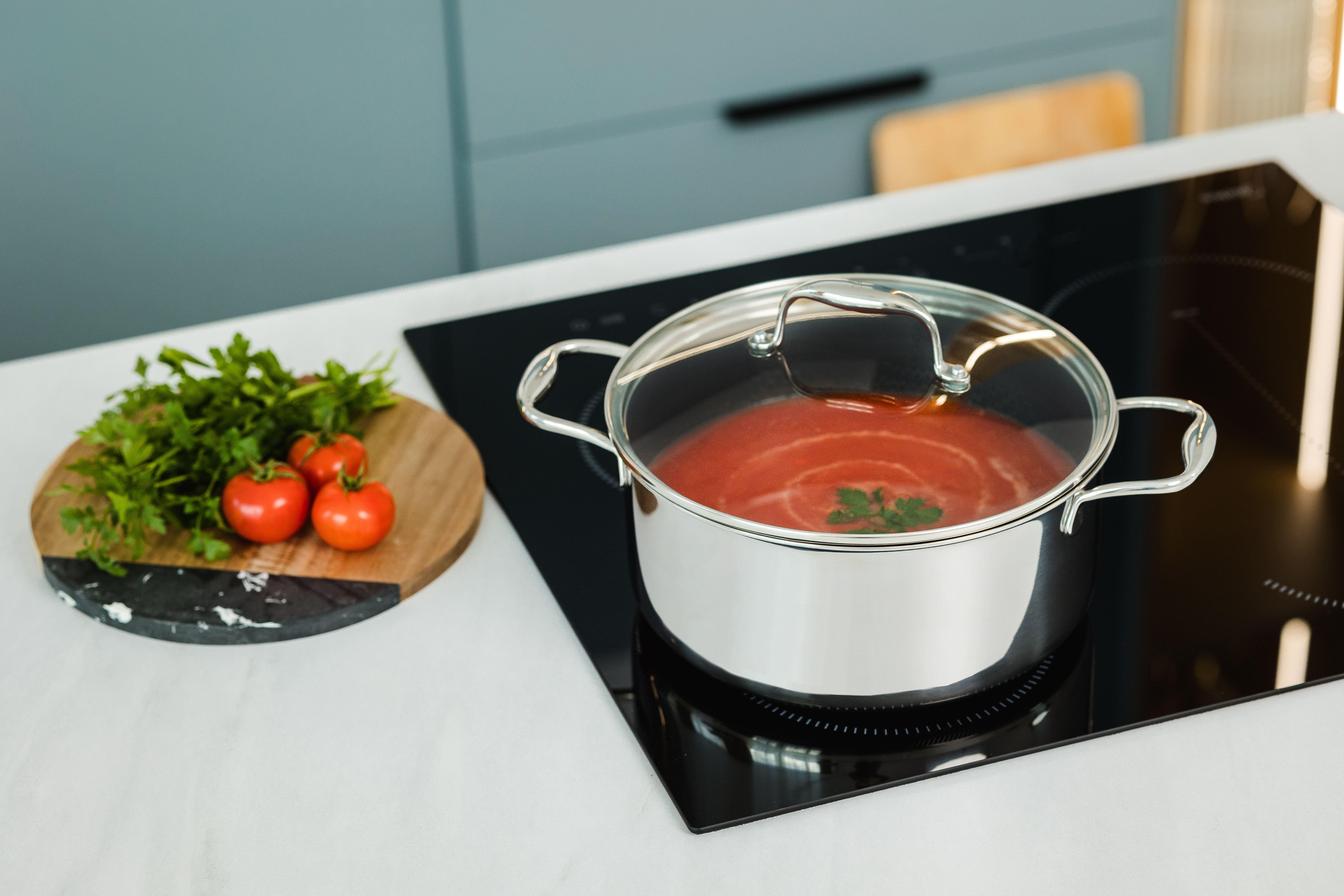 Garnek z sosem pomidorowym na kuchence, obok pietruszki i pomidorów.