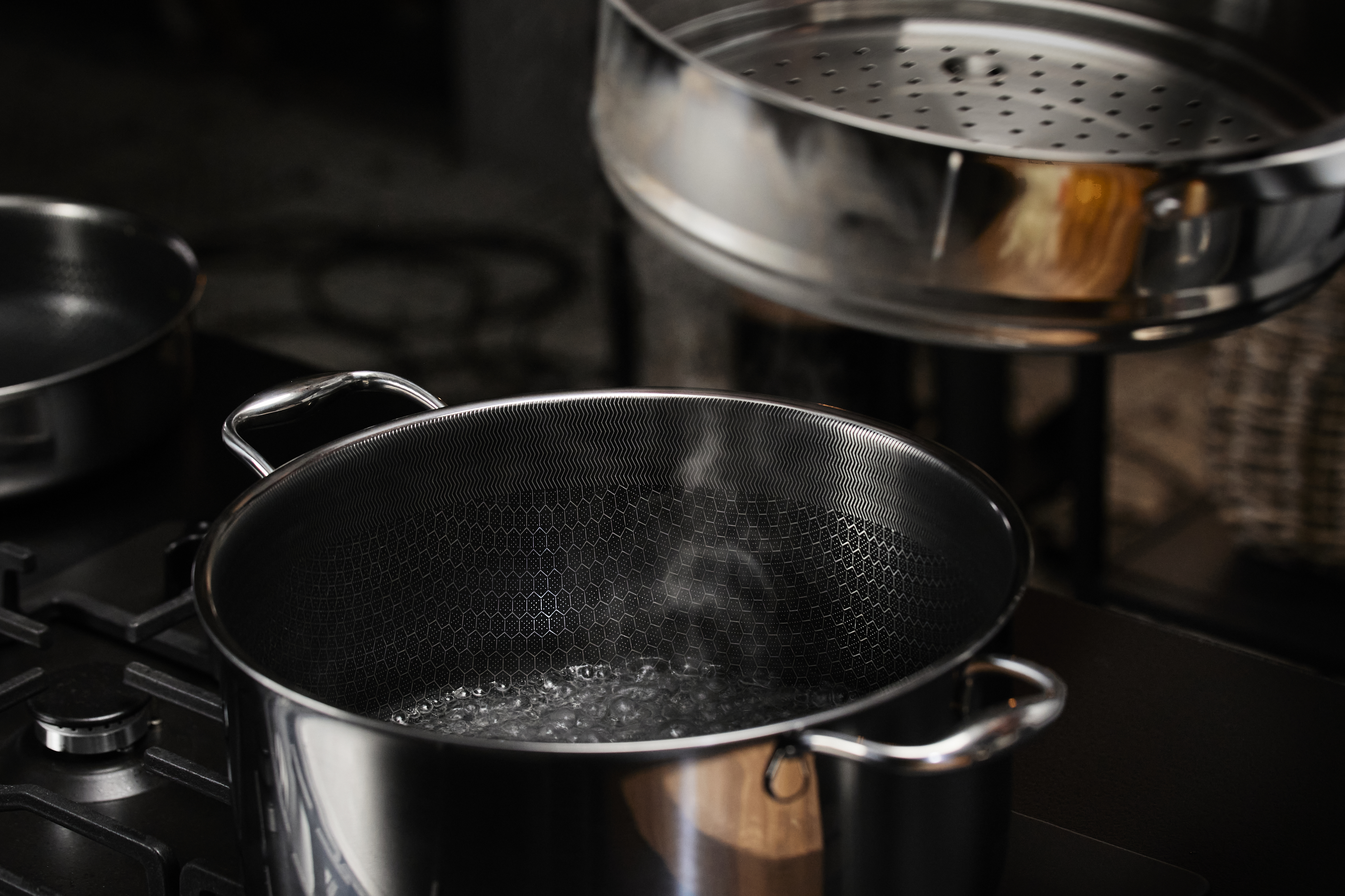 Garnek ze stali nierdzewnej z wrzącą wodą na kuchence. Nad nim widoczny jest kosz do gotowania na parze.