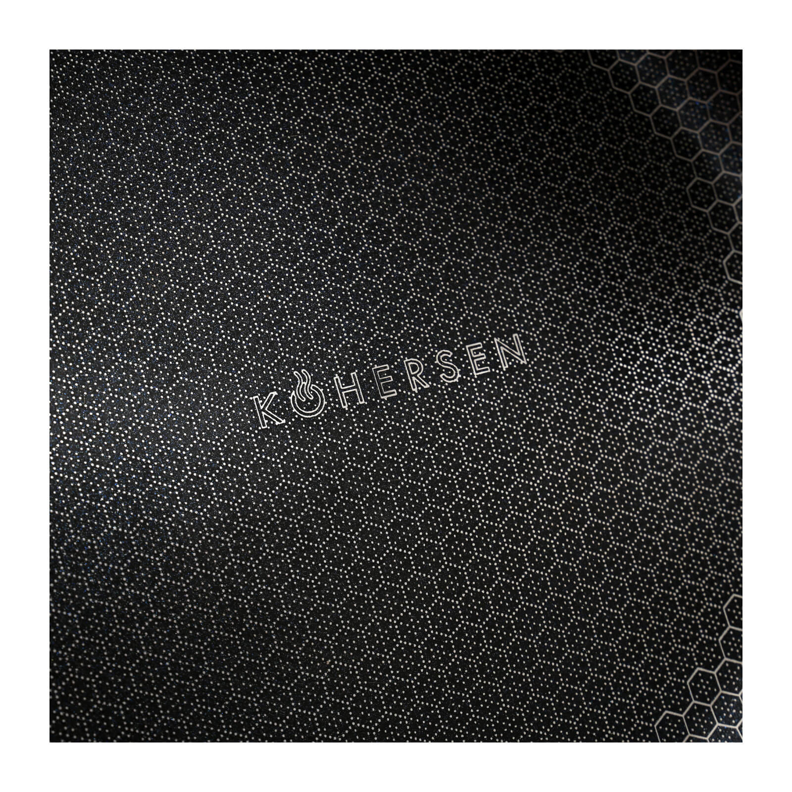 Zbliżenie czarnej patelni z teksturowaną powierzchnią i białym napisem 'KOHERSEN'.