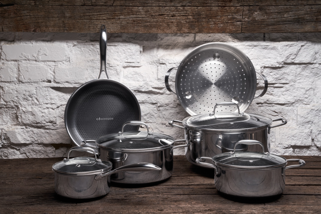 Garnki kuchenne na drewnianym stole. Ułożono patelnię, parowar i garnki o różnych rozmiarach.