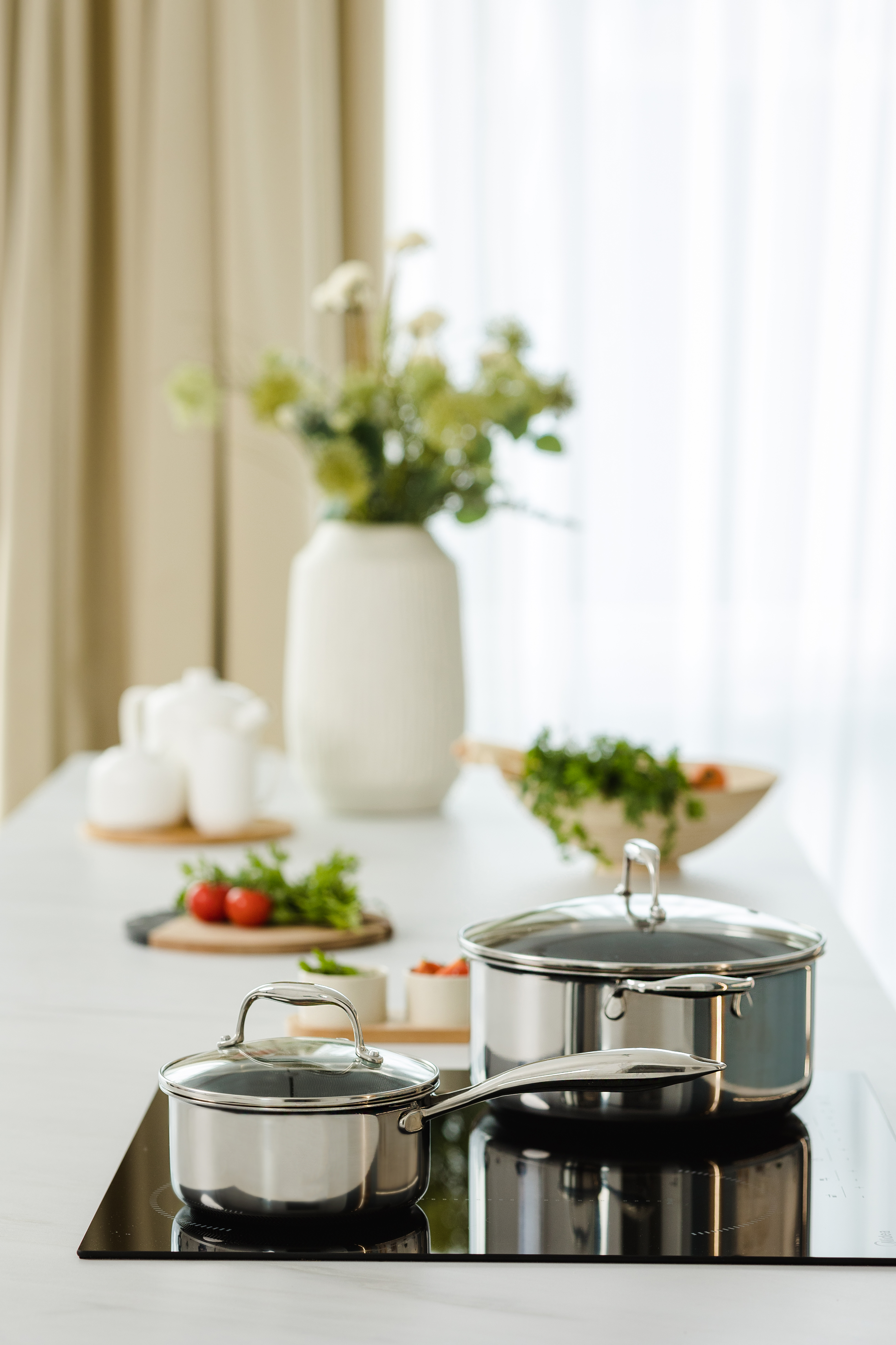 Scena kuchenna ze stalowymi garnkami na czarnej płycie i warzywami.