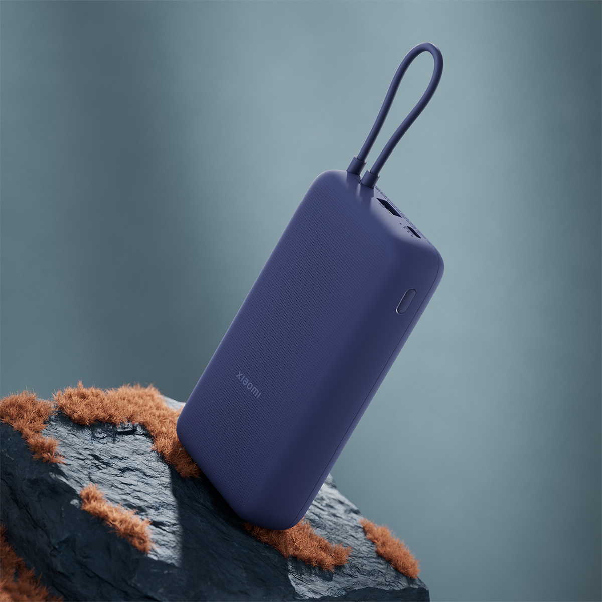 Kék Xiaomi powerbank pánttal, textúrázott kőre helyezve, elmosódott háttér előtt.