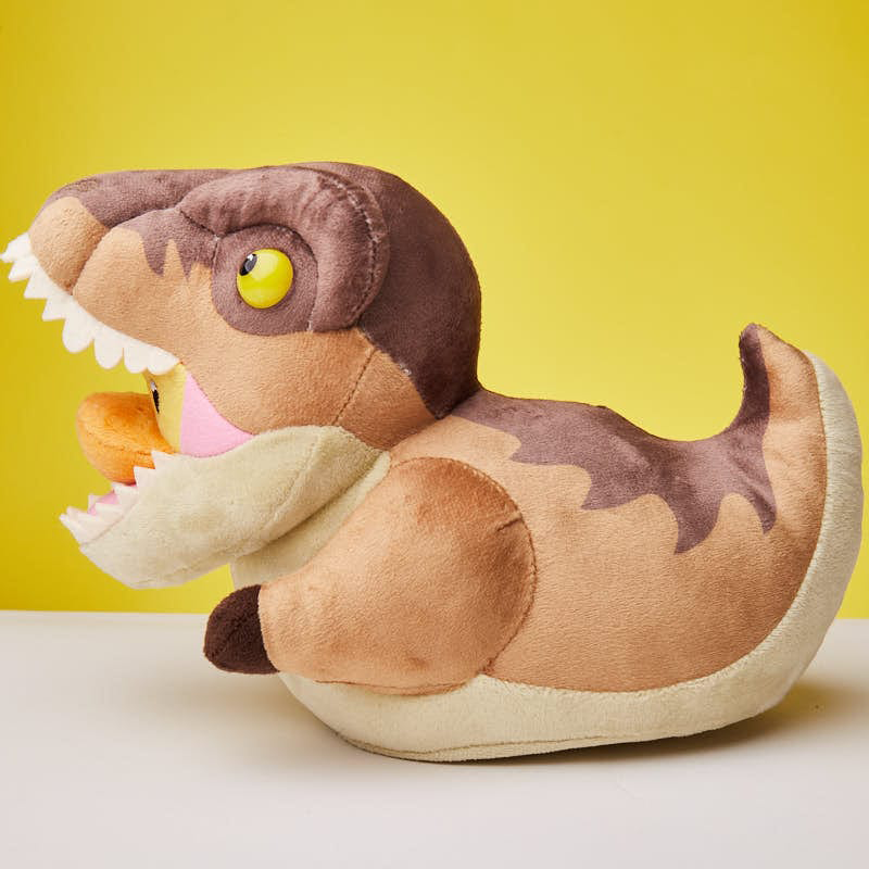 Barna és barna plüss dinoszaurusz játék, fehér fogakkal, fehér felületen, sárga háttérrel.