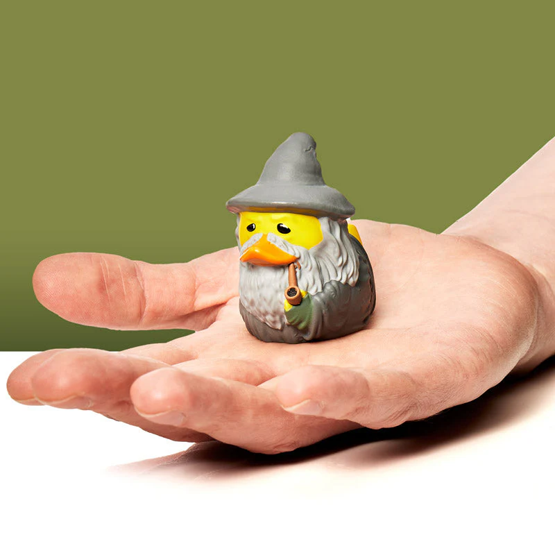Egy gumikacsa, szürke kalapban és szakállal, varázslónak öltözve. Egy kézben van, zöld háttérrel.