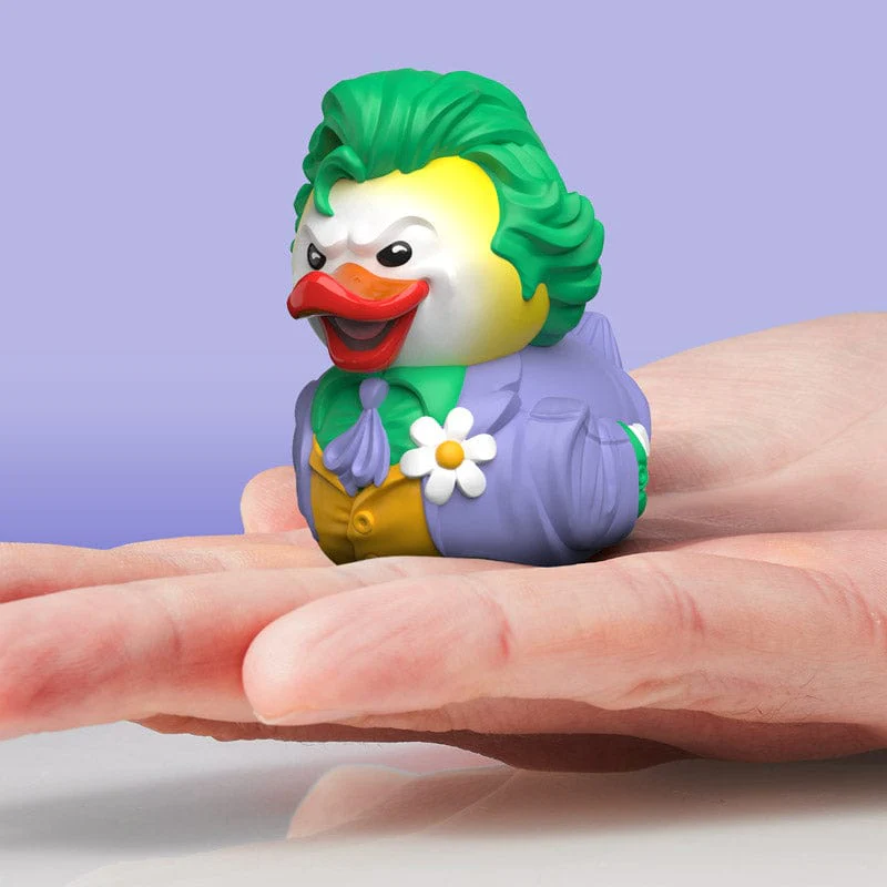 A Joker gumikacsa játék. A játékot egy kézben tartják, lila háttérrel.