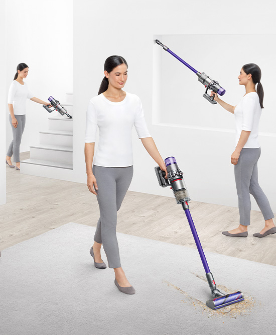 Kobieta odkurza dywan fioletowym odkurzaczem.