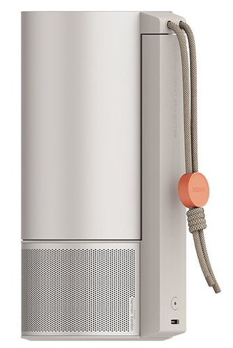Widok z boku cylindrycznego głośnika Harman Kardon z paskiem do przenoszenia i pomarańczowym przyciskiem.