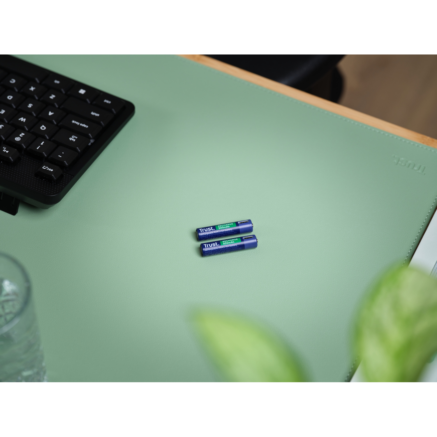 Deux piles AA, étiquettes bleues et vertes, sur un tapis de bureau vert, près d'un clavier noir.
