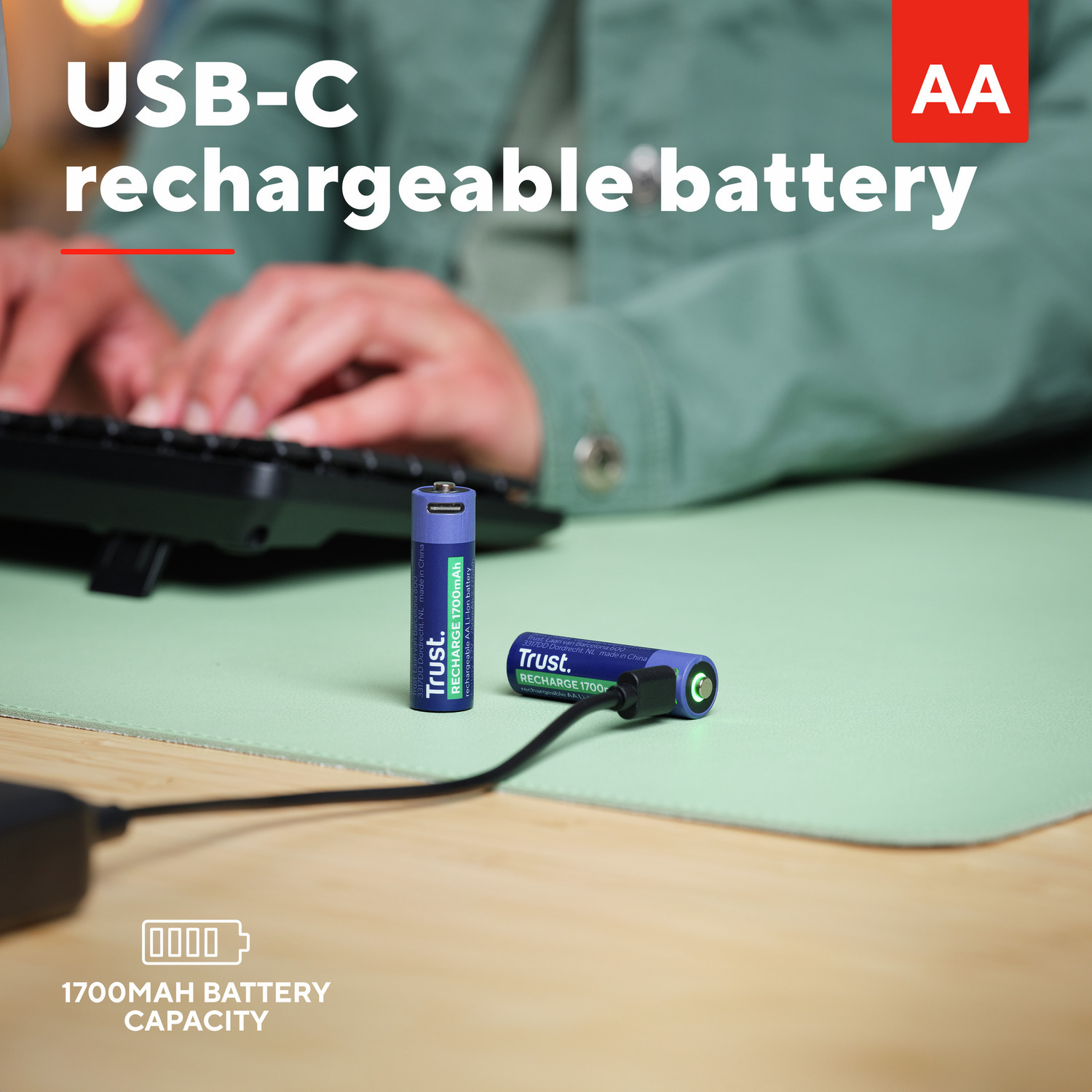 Een USB-C oplaadbare AA-batterij wordt opgeladen op een groen bureau met een toetsenbord.