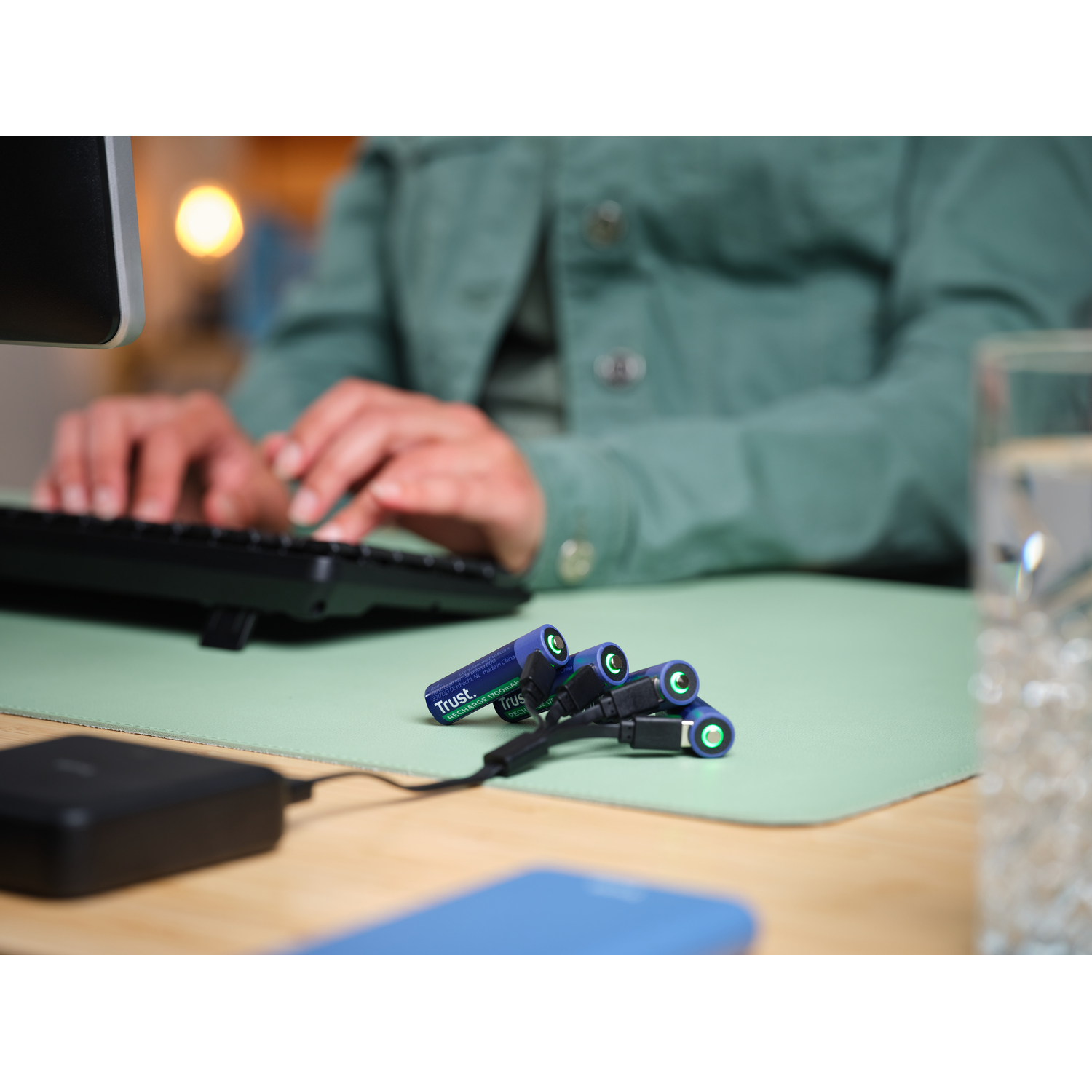 Persoon die batterijen oplaadt met een oplader op een groene mat, met een laptop op de achtergrond.