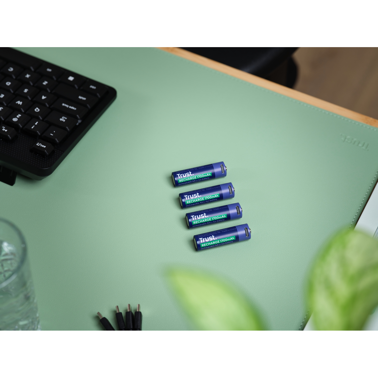 Vier blauwe Trust Recharge 1700mAh batterijen liggen op een groen bureau.