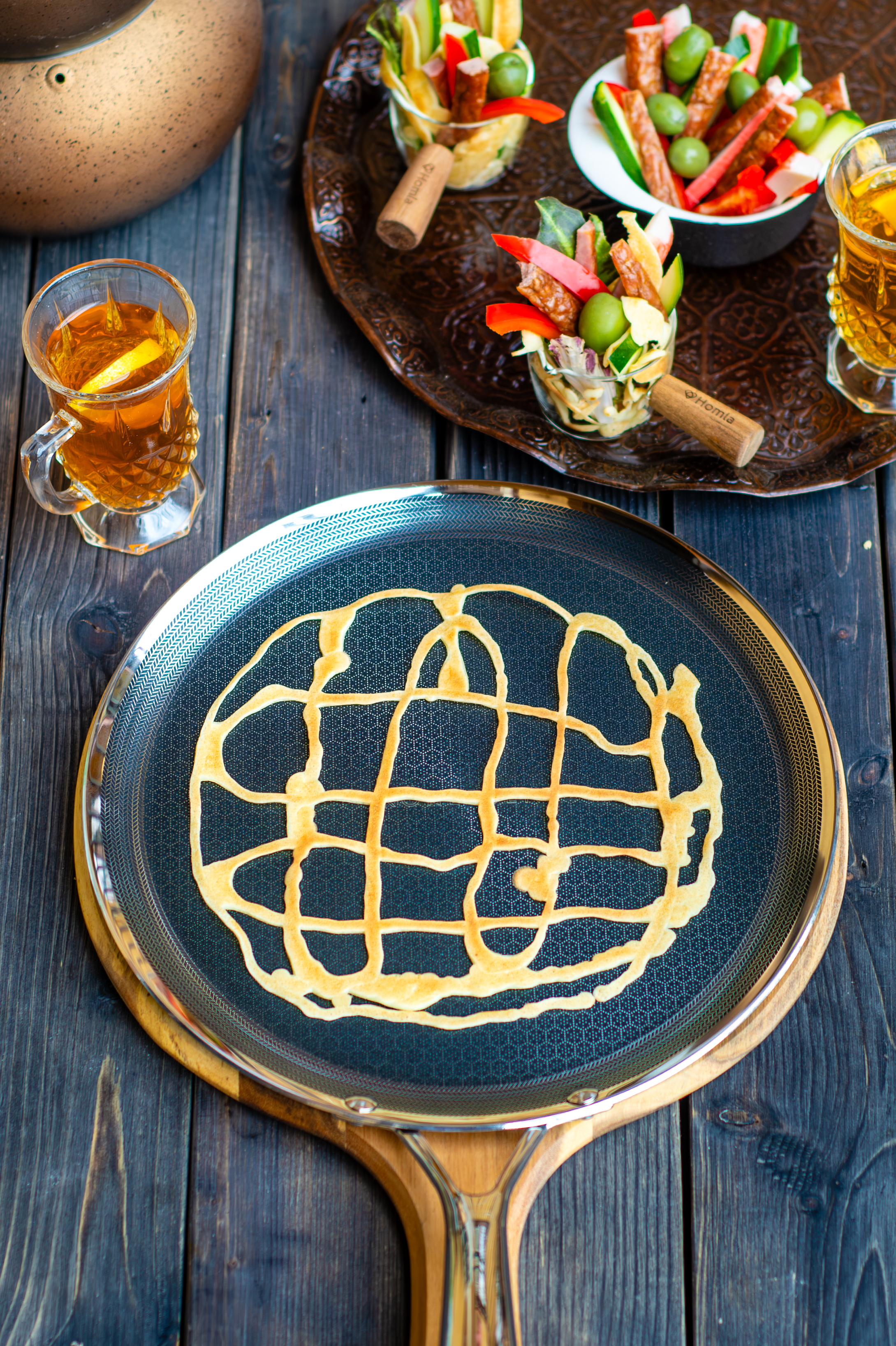 Patelnia z jedzeniem i szklanka z płynem. Inne potrawy w tle. Na ciemnej drewnianej powierzchni.