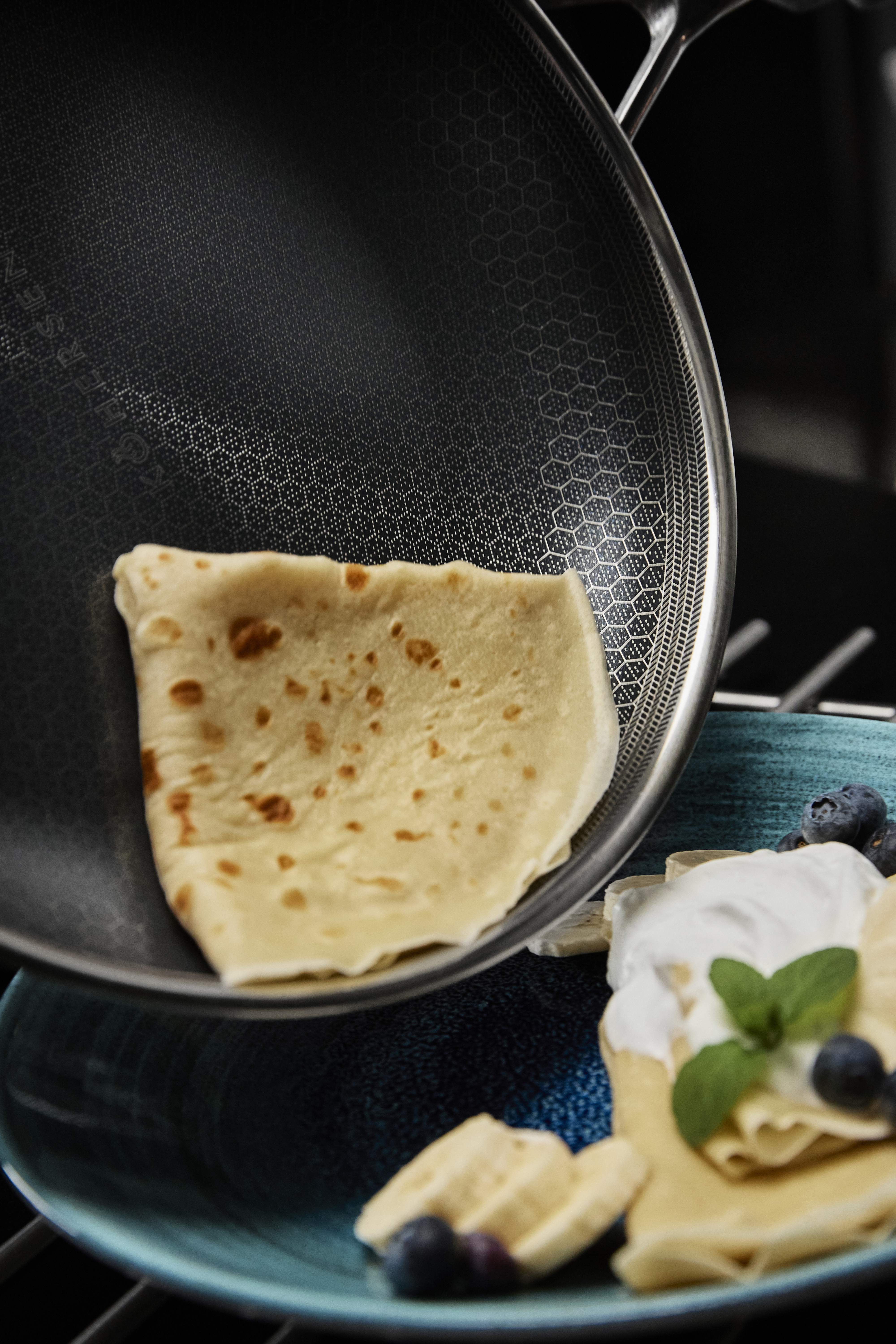 Naleśnik podnoszony z patelni. Niebieski talerz z owocami i kremem.