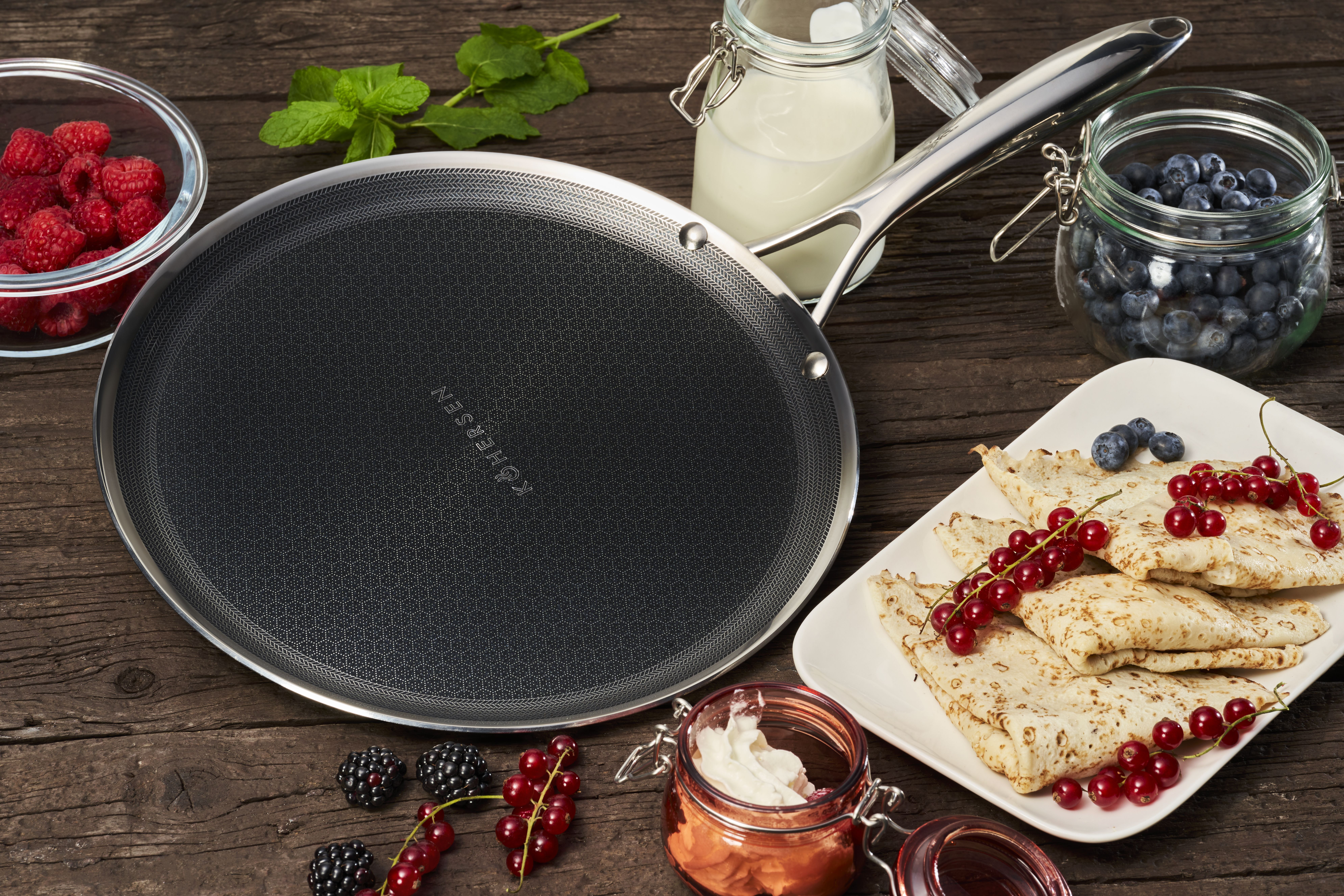 Patelnia do naleśników z naleśnikami, jagodami i śmietaną na drewnianym stole. Słoiki z borówkami i mlekiem.