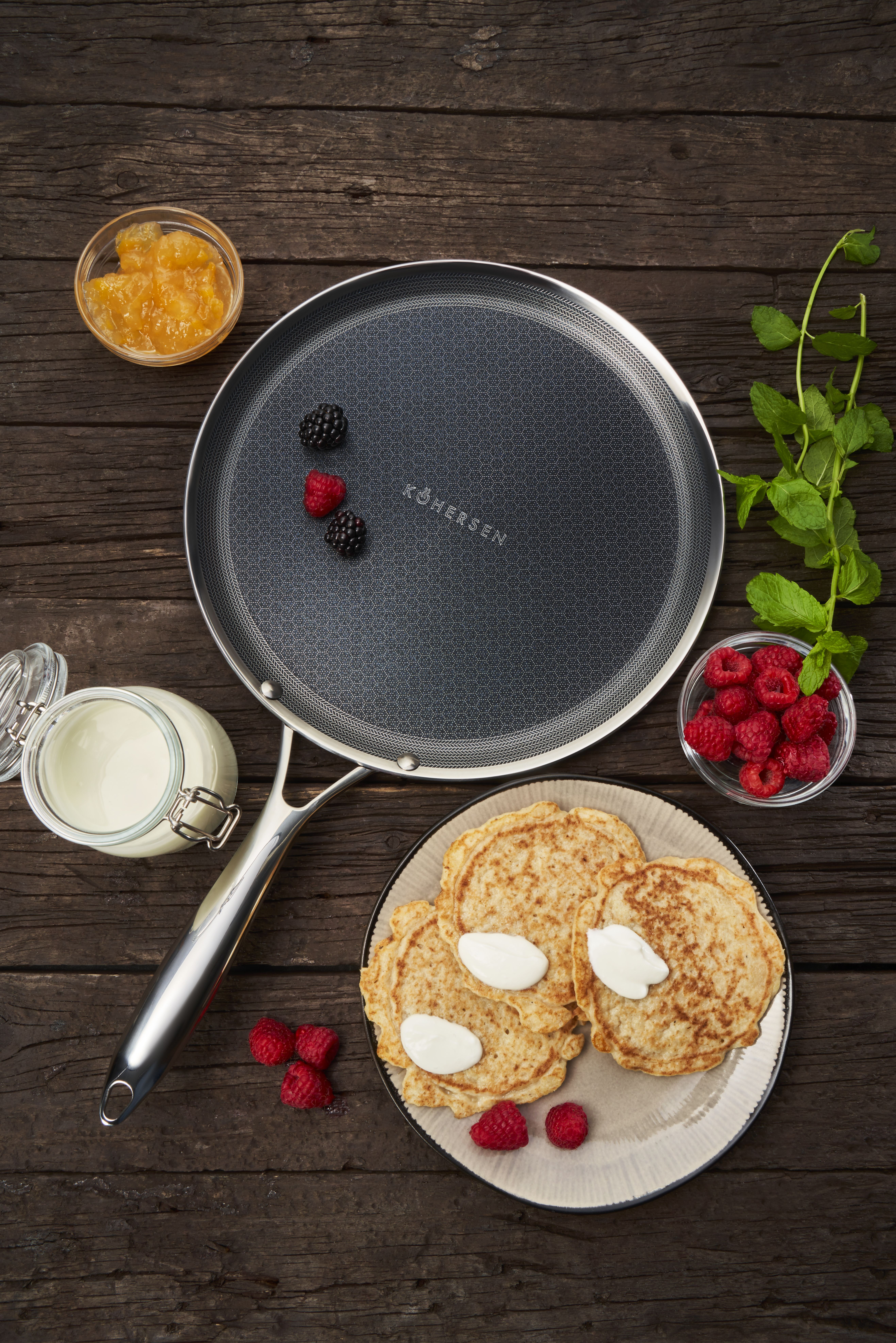 Naleśniki ze śmietaną i malinami na drewnianym stole z miętą i dżemem.