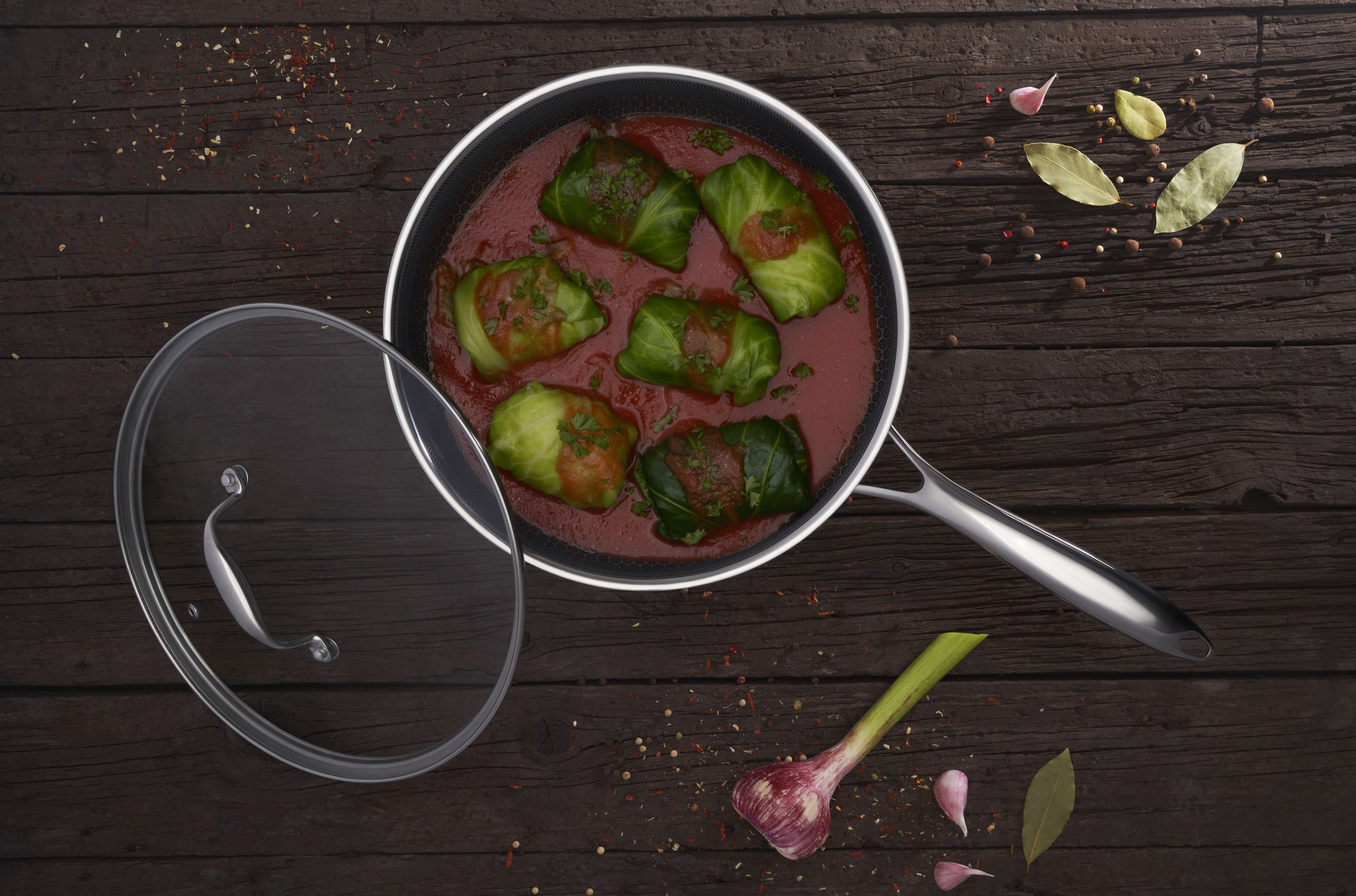 Patelnia z gołąbkami w sosie pomidorowym na drewnianej powierzchni, z pokrywką i czosnkiem.
