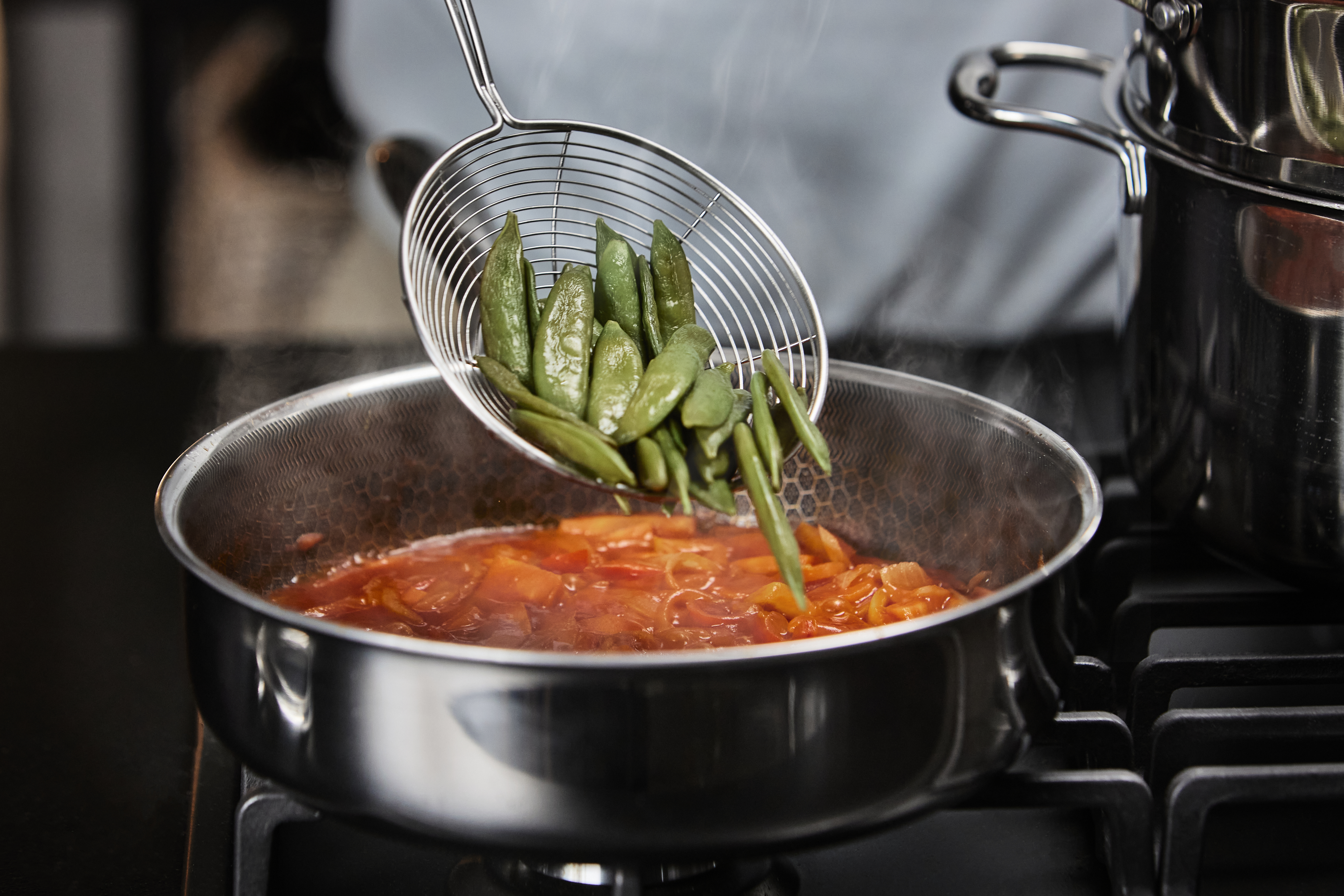 Zielony groszek cukrowy jest nabierany z garnka łyżką szczelinową do patelni.