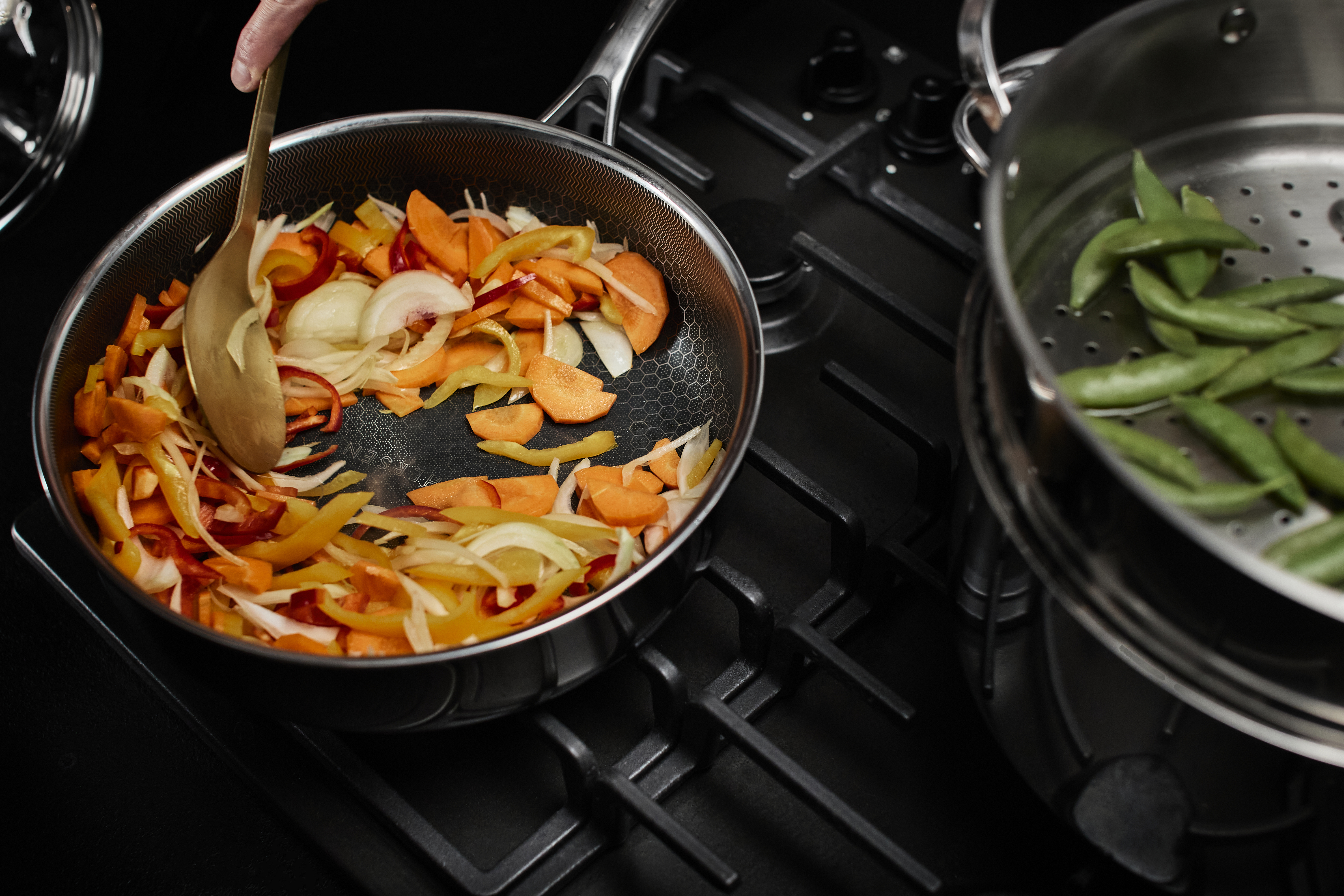 Patelnia na kuchence z gotowanymi warzywami i parowar z boku.