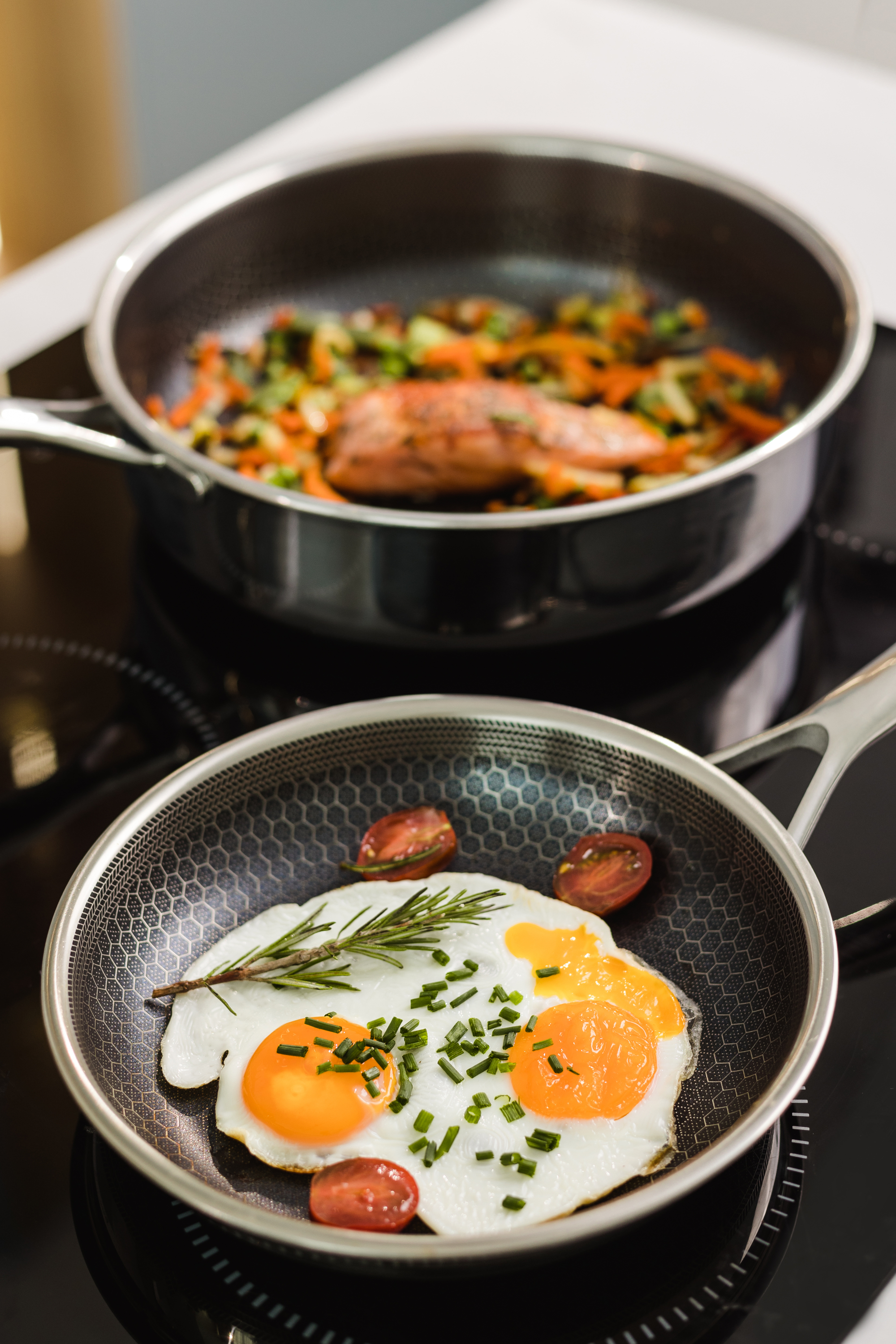 Dwie patelnie z jedzeniem na kuchence. Jajka sadzone i warzywa. Widok z góry.