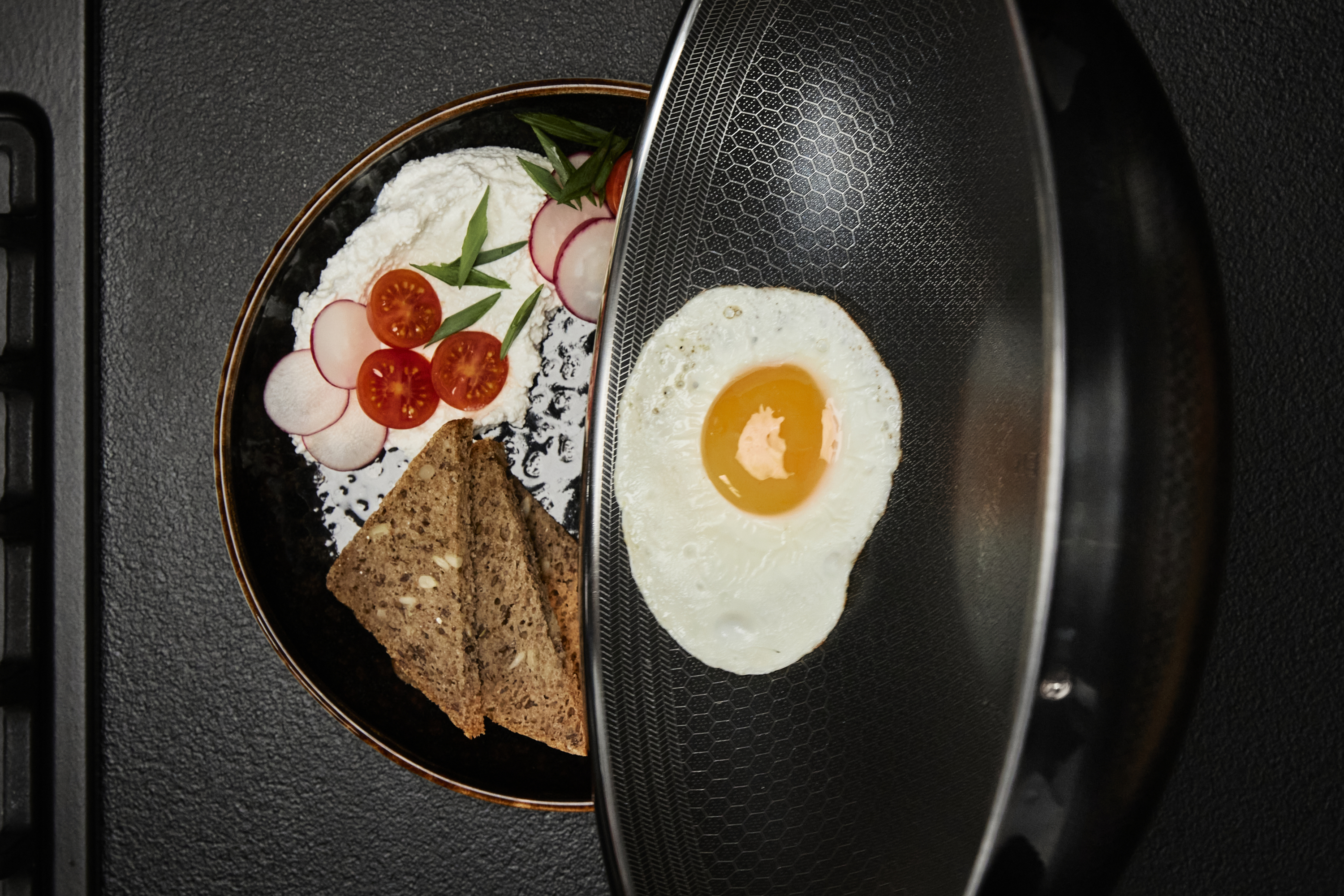 Talerz z jedzeniem, w tym chlebem, pomidorami i jajkiem. Patelnia o wzorze plastra miodu.