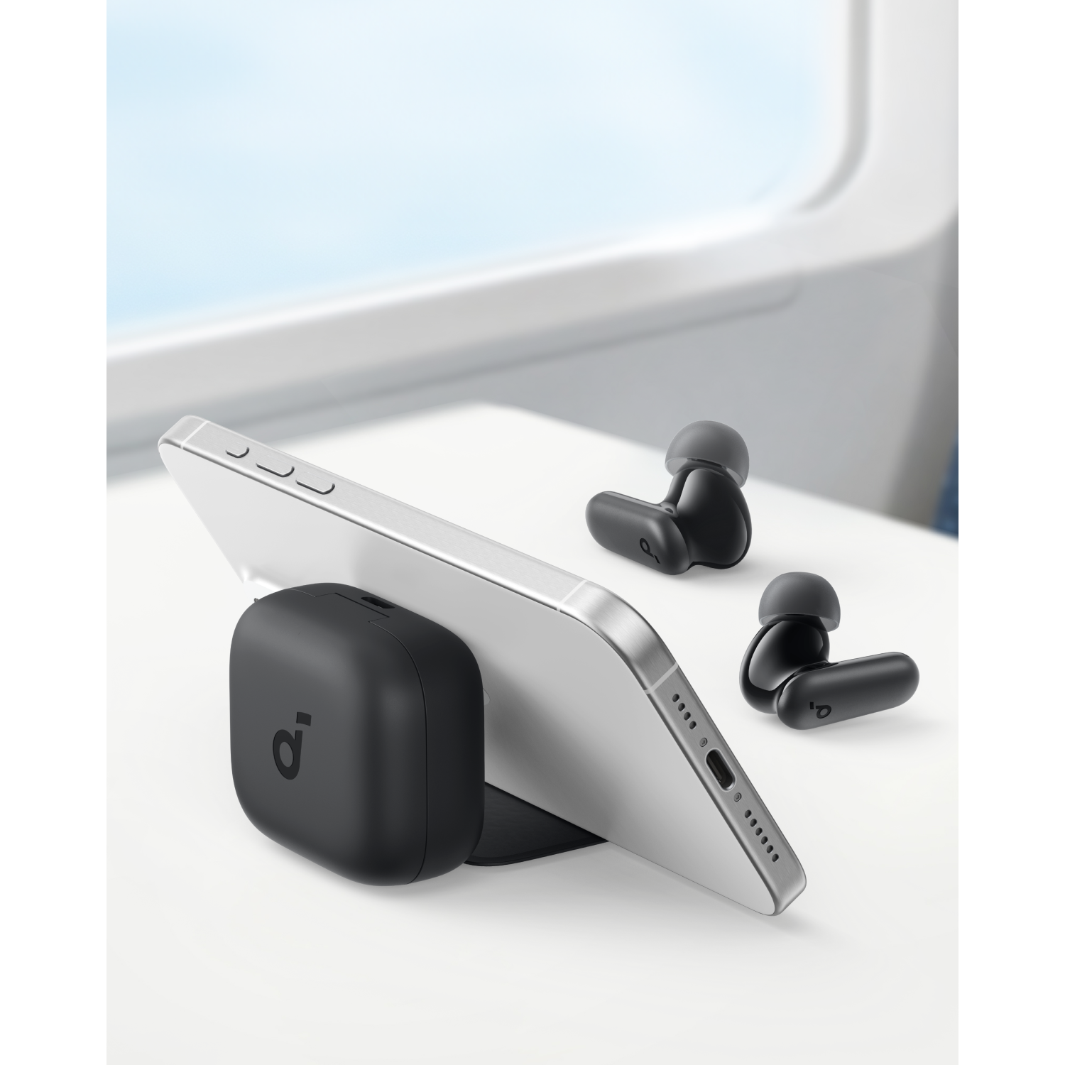 A phone propped up by a black charging stand. Wireless earbuds are next to the phone.