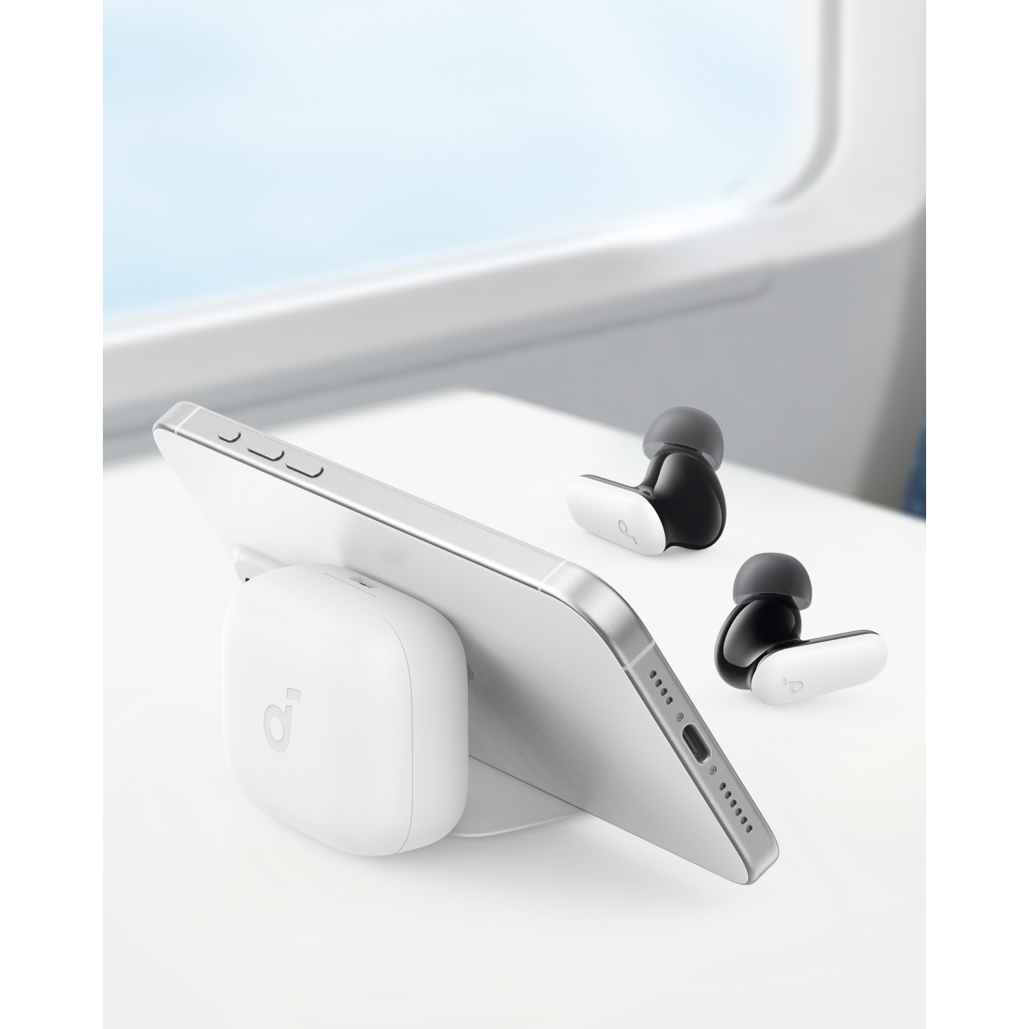 Telefoon op witte standaard met oortelefoons. Achtergrond: raam en witte tafel.