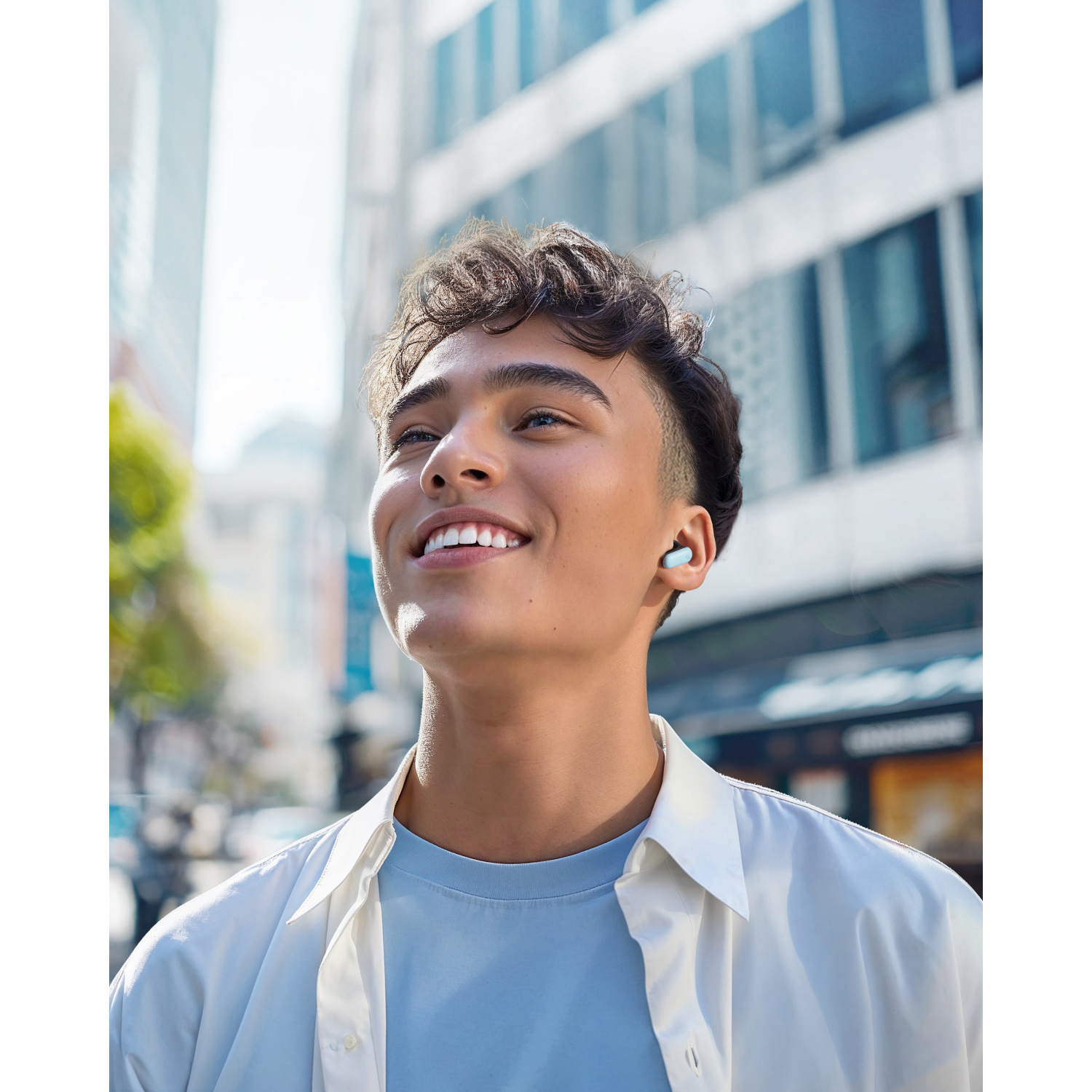 A young man looking up, wearing earbuds and standing on a city street.