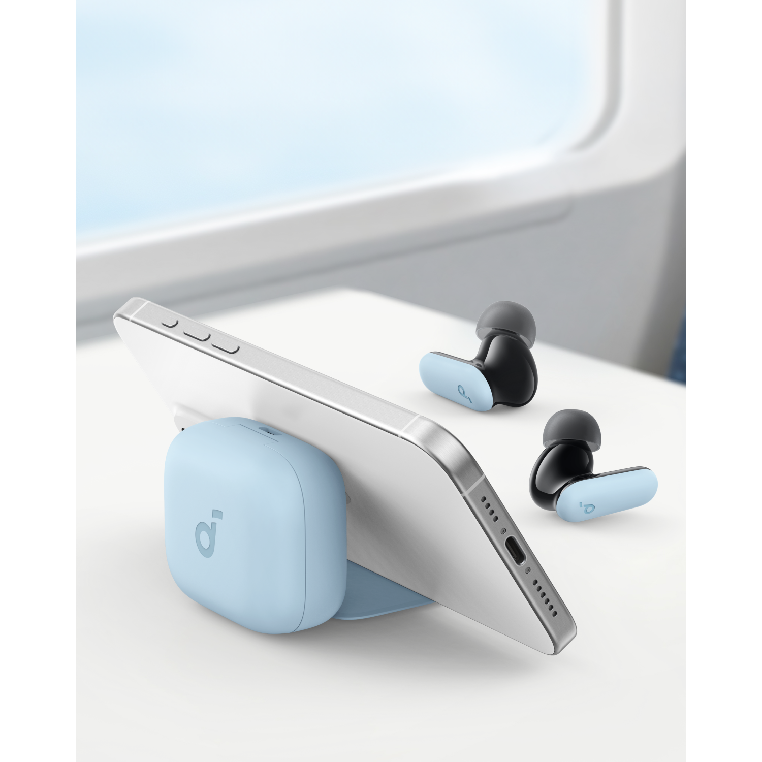 Phone on stand with earbuds and a light blue charger. All on a table.