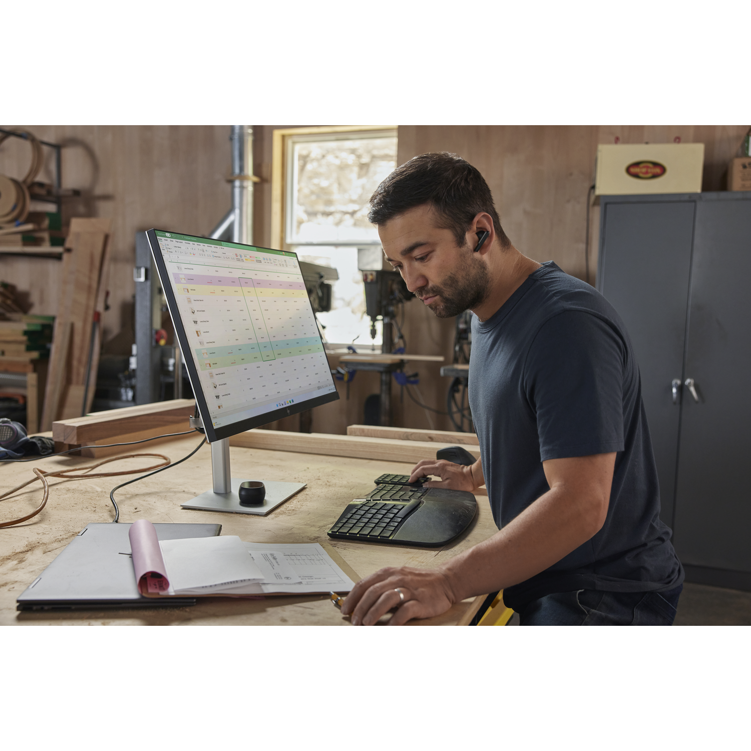 Man die aan een bureau werkt. Laptop, monitor, toetsenbord en koptelefoon. Kantooromgeving.