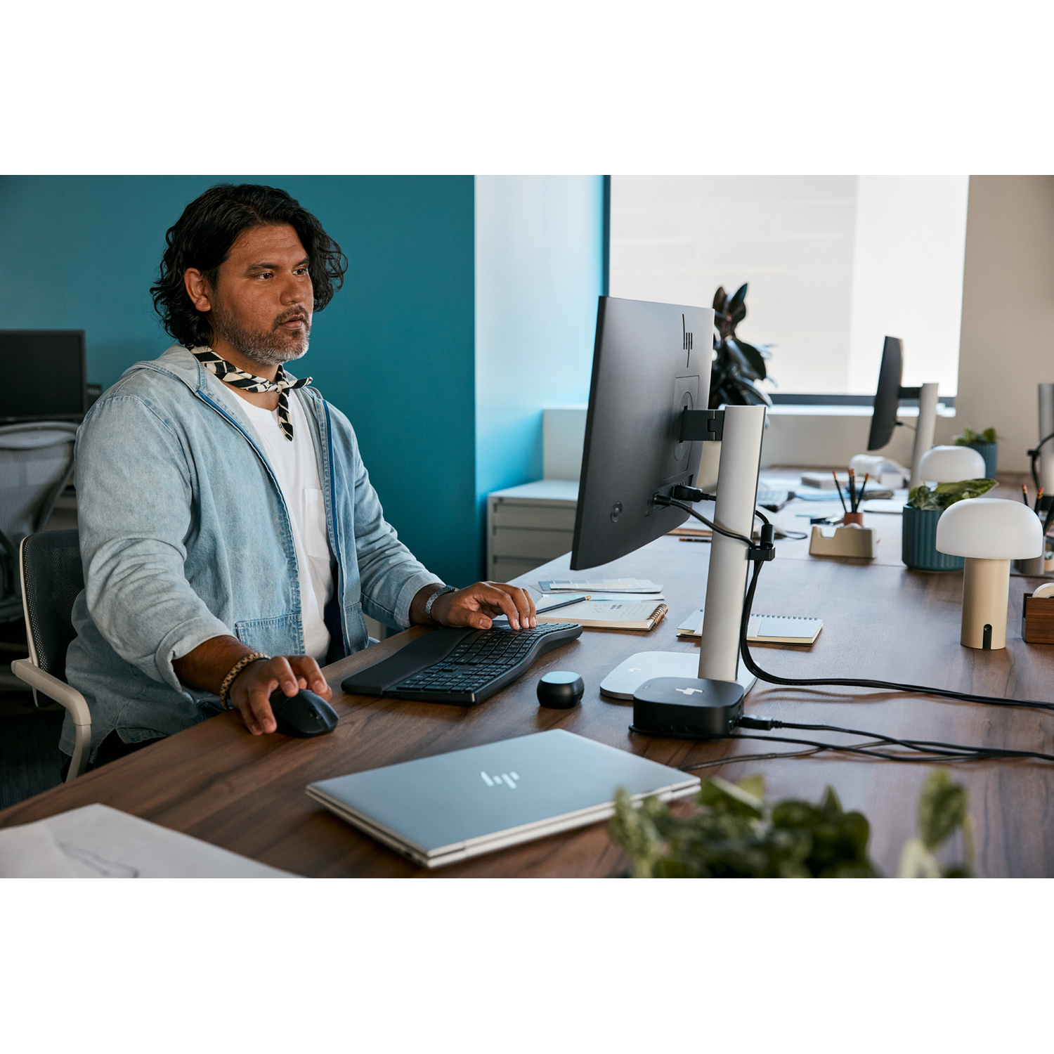 Een man aan een bureau die op een computer werkt. Een monitor en andere accessoires bevinden zich in de werkruimte.