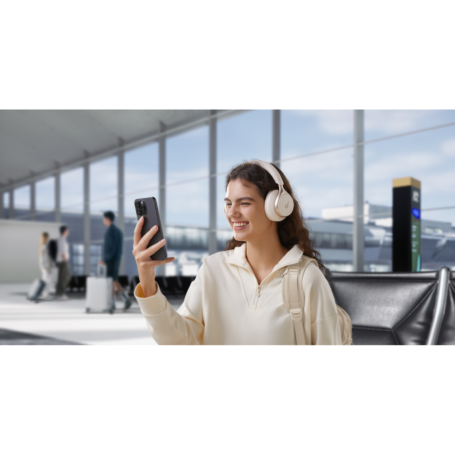 Femme à l'aéroport utilisant un casque et un téléphone, souriante, avec arrière-plan.