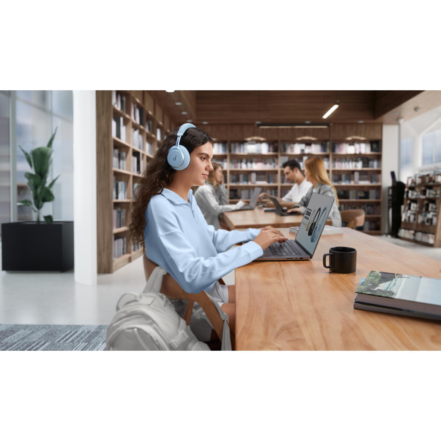 Een vrouw met een koptelefoon gebruikt een laptop. Andere mensen zijn op de achtergrond.